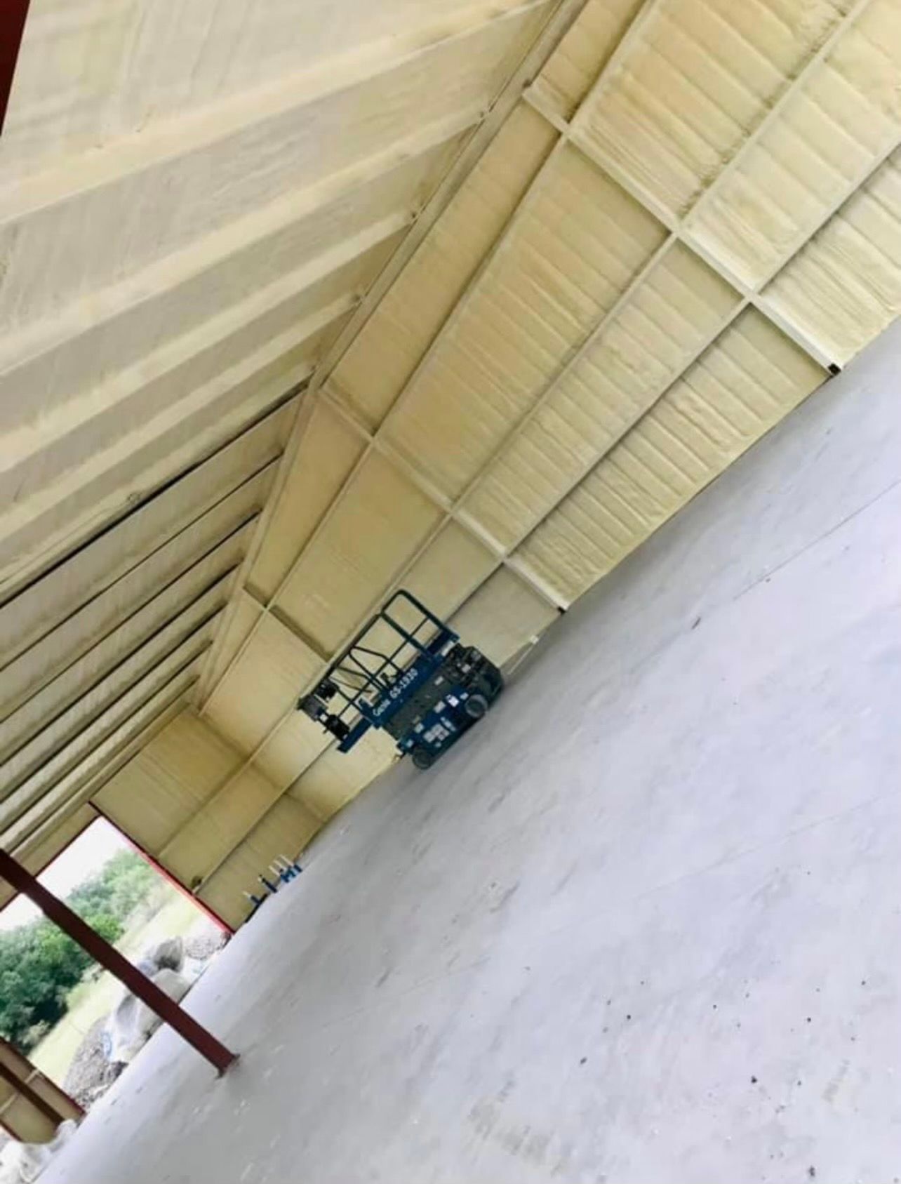 Interior of a building with a white spray-foam insulated roof, concrete floor, and a small vehicle.