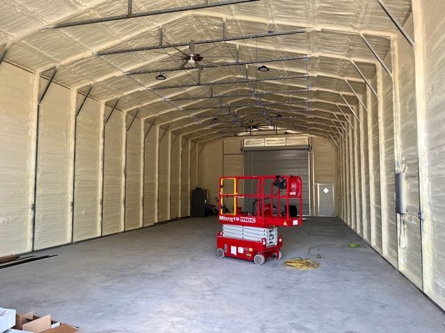 Interior of a tan spray-foam insulated warehouse; red lift, gray concrete floor.