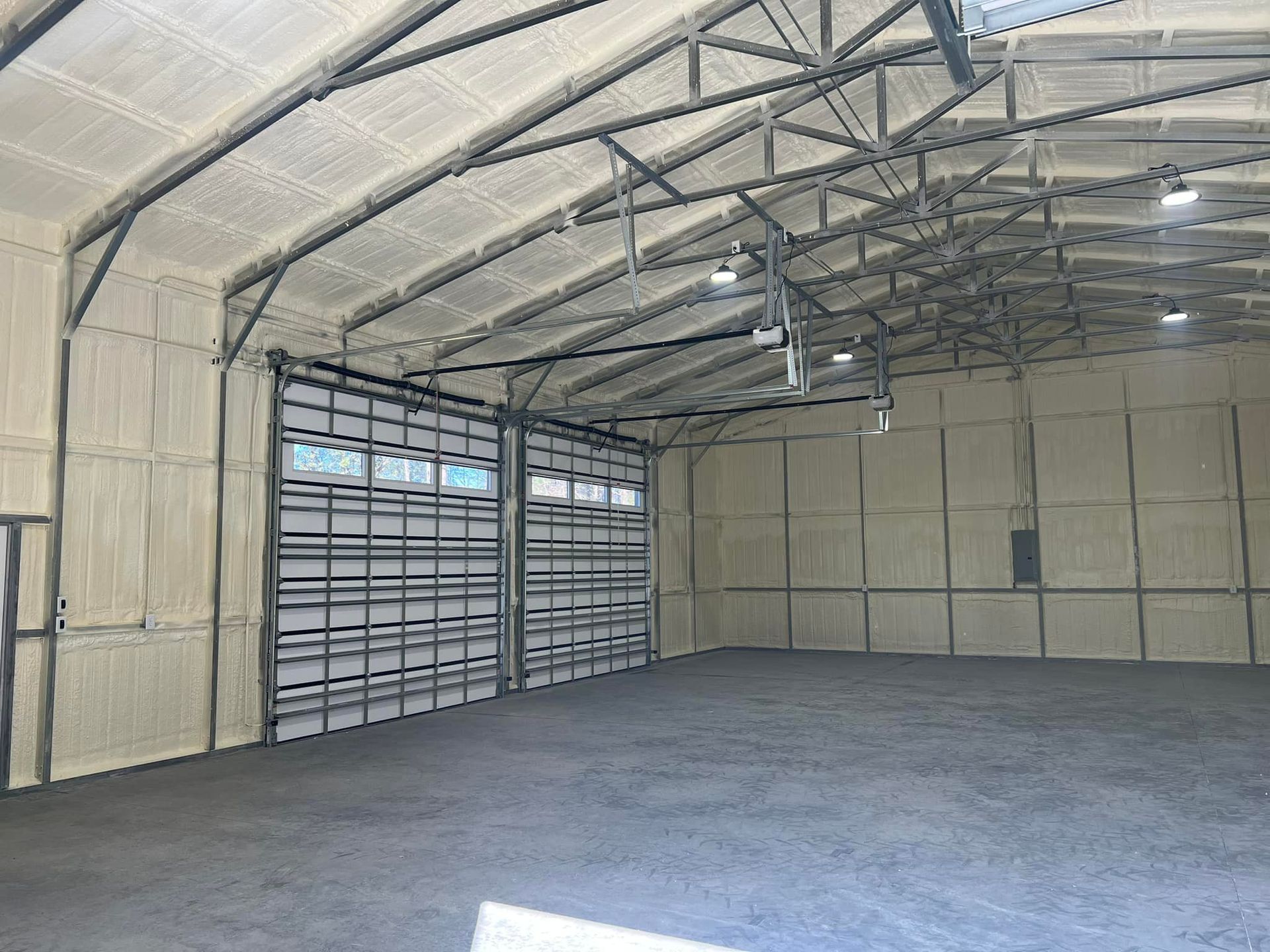 Interior of a large warehouse with gray concrete floor, spray foam insulation, and metal framed doors and ceiling.