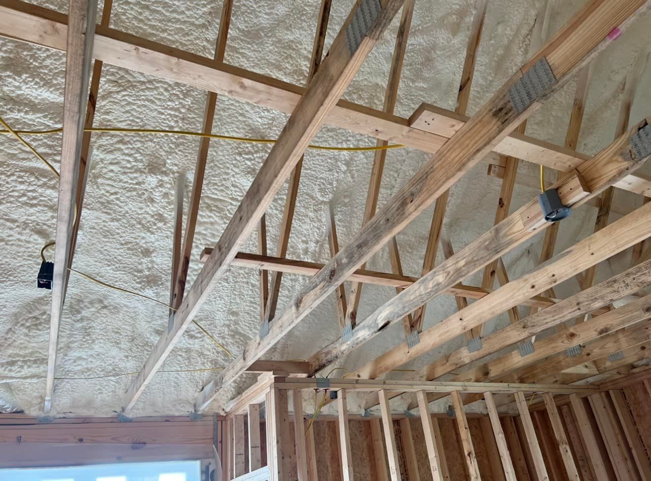 Wooden ceiling structure with spray foam insulation. Yellow electrical wire runs across.