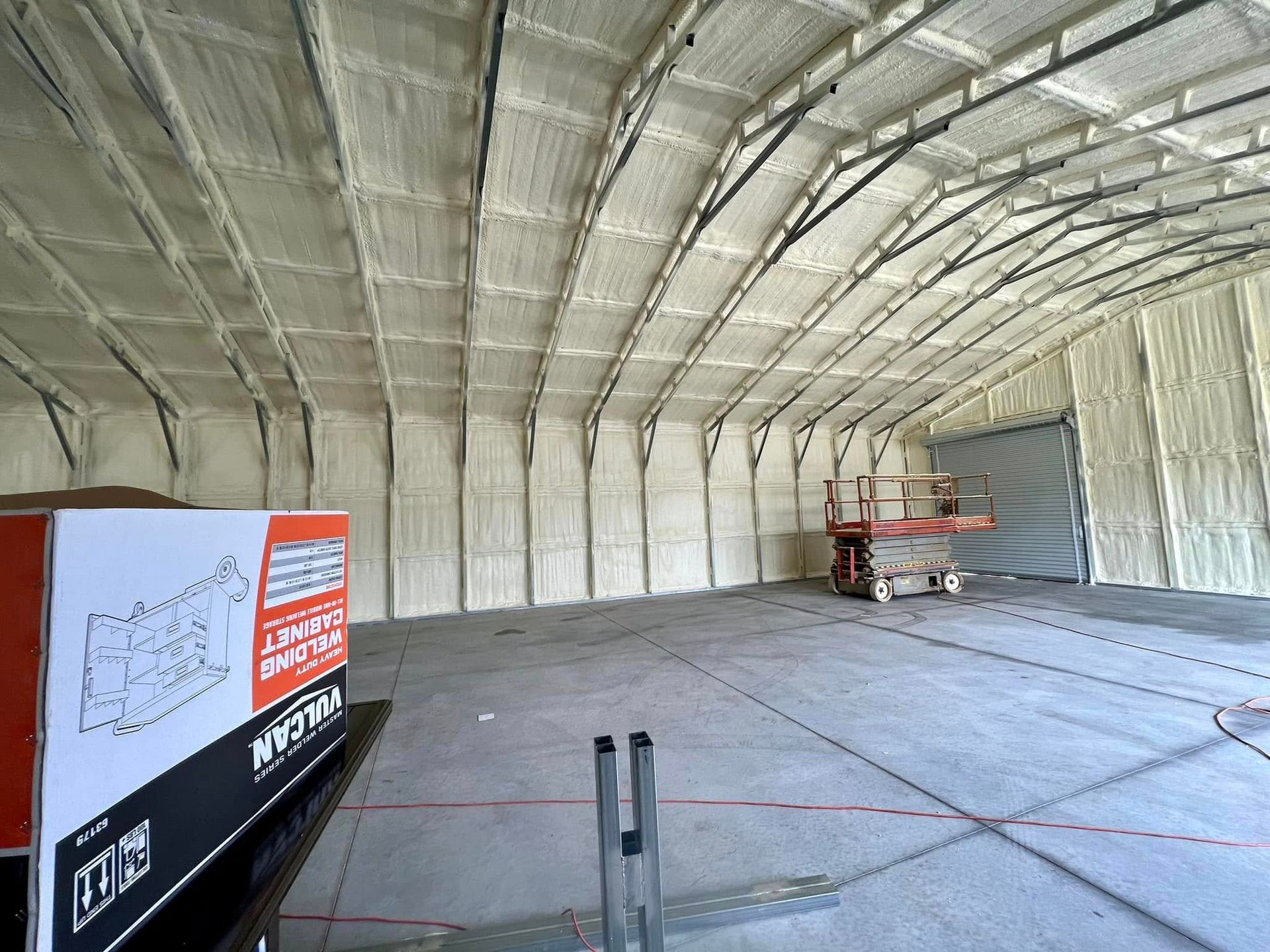 Interior of a large building with spray foam insulation on walls and ceiling, empty space, lift in the distance.