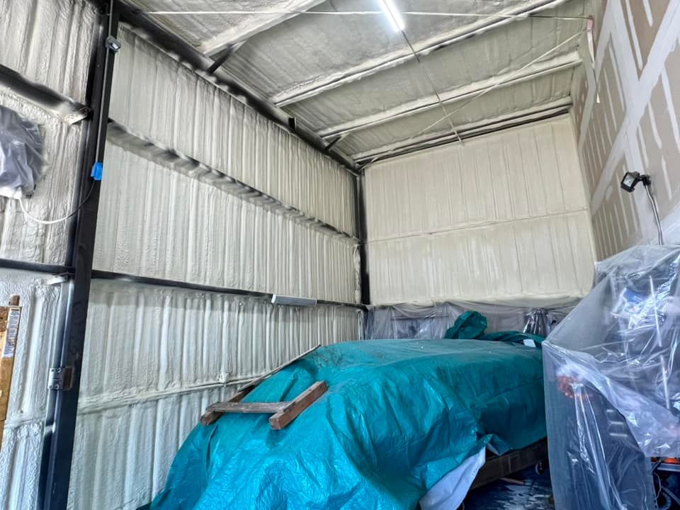 Interior view of a building's metal walls and ceiling insulated with white foam; a tarp-covered object is inside.