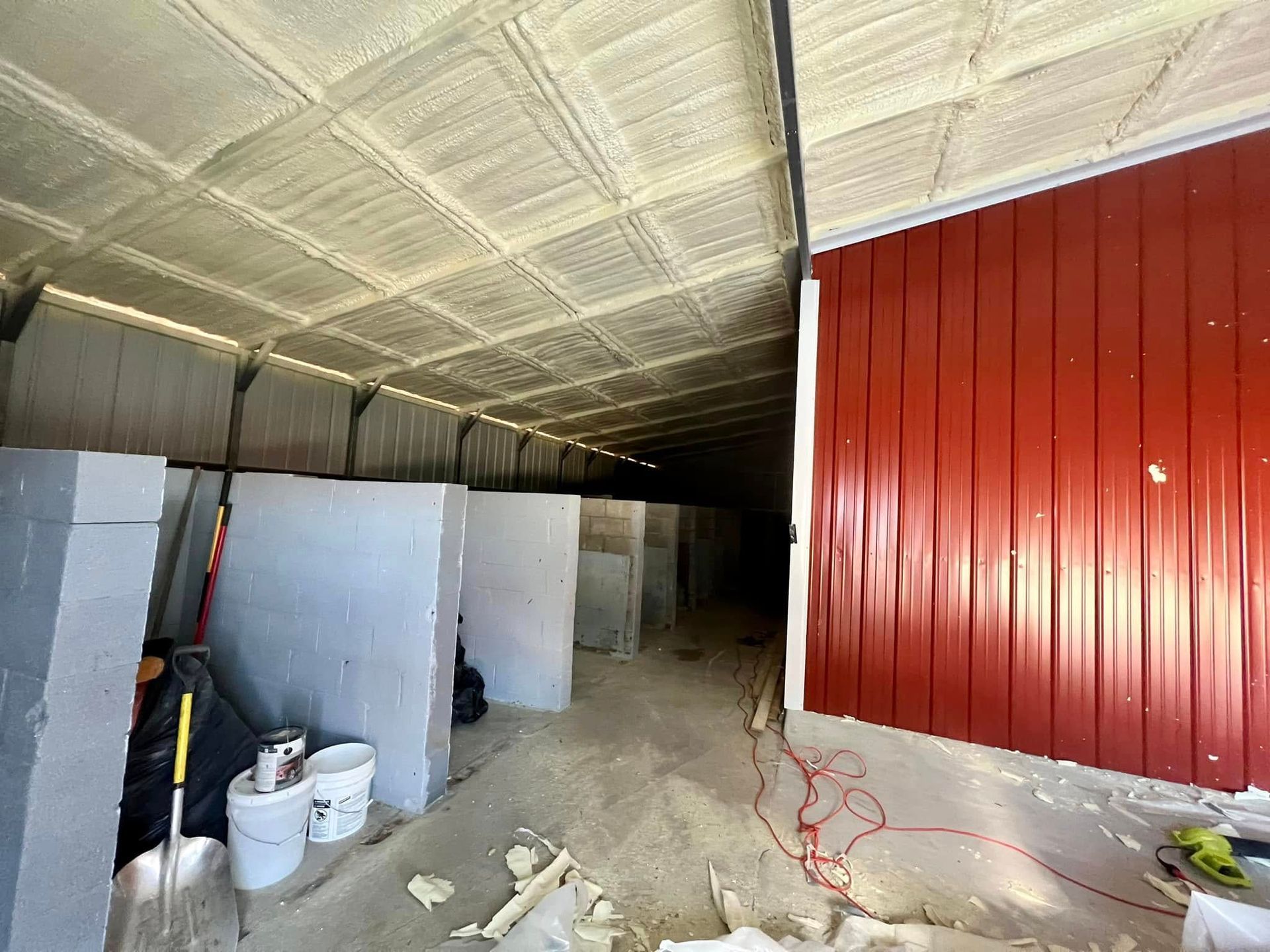 Interior of a building with red metal siding and a spray-foam ceiling; walls are being constructed.