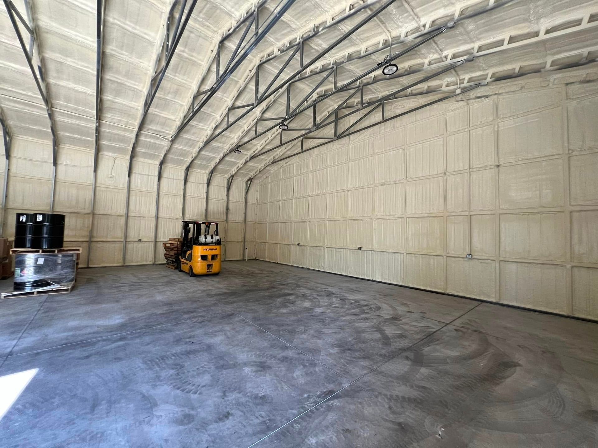 Interior of a large warehouse insulated with spray foam. A forklift sits inside, along with pallets and barrels.