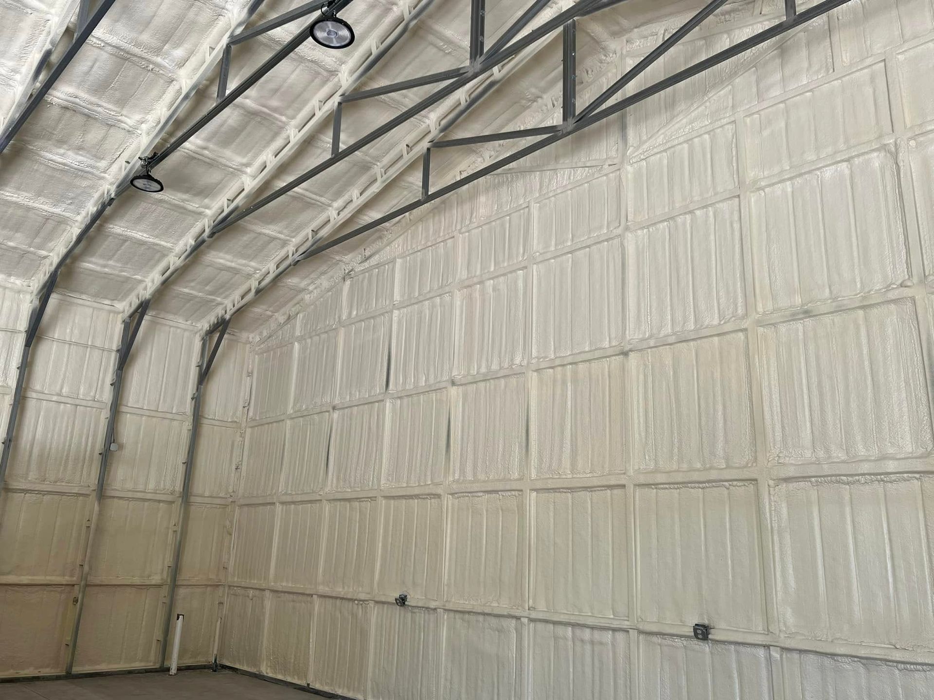 Interior view of a building with spray foam insulation on the walls and arched ceiling. Metal framing is visible.