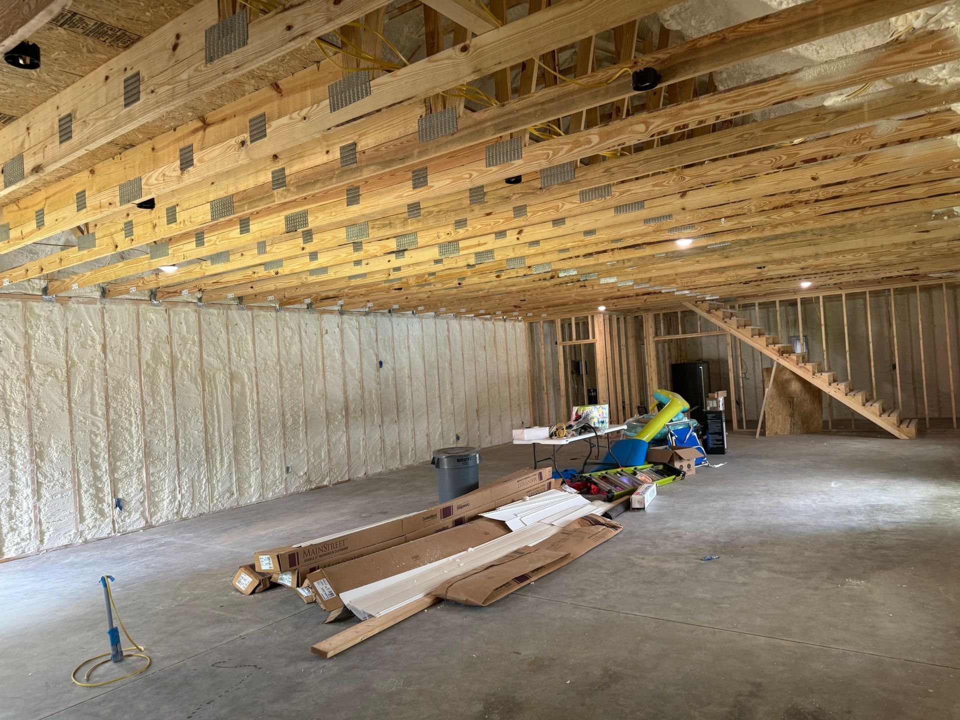 Unfinished interior with spray foam insulation on the left wall, exposed beams, and concrete floor.