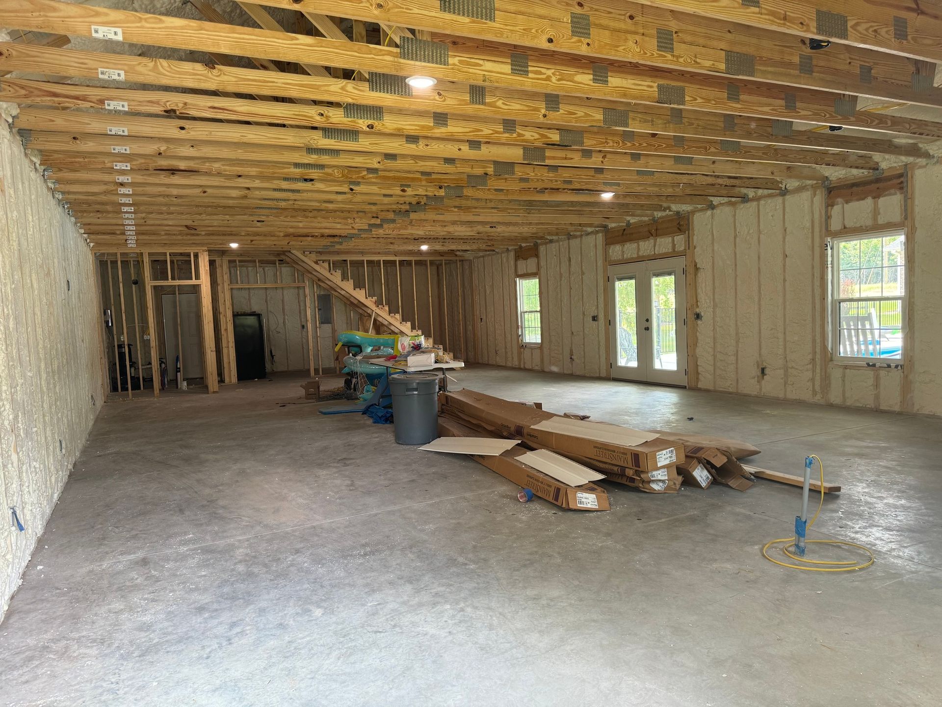 Interior of a building under construction, featuring exposed wooden beams, concrete floor, and partially framed walls.