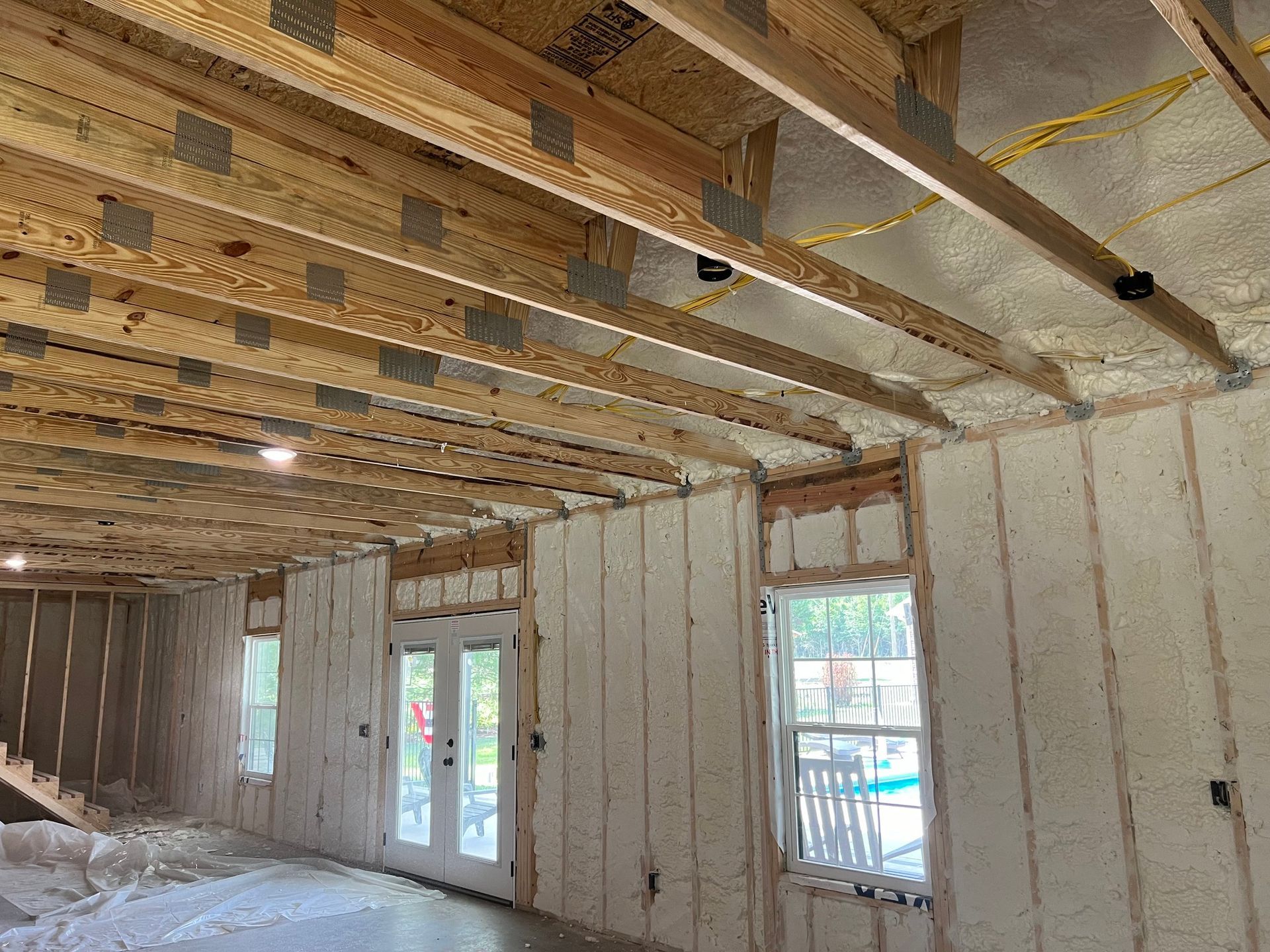Interior of a building under construction, insulated with spray foam. Wooden beams and window frames are visible.
