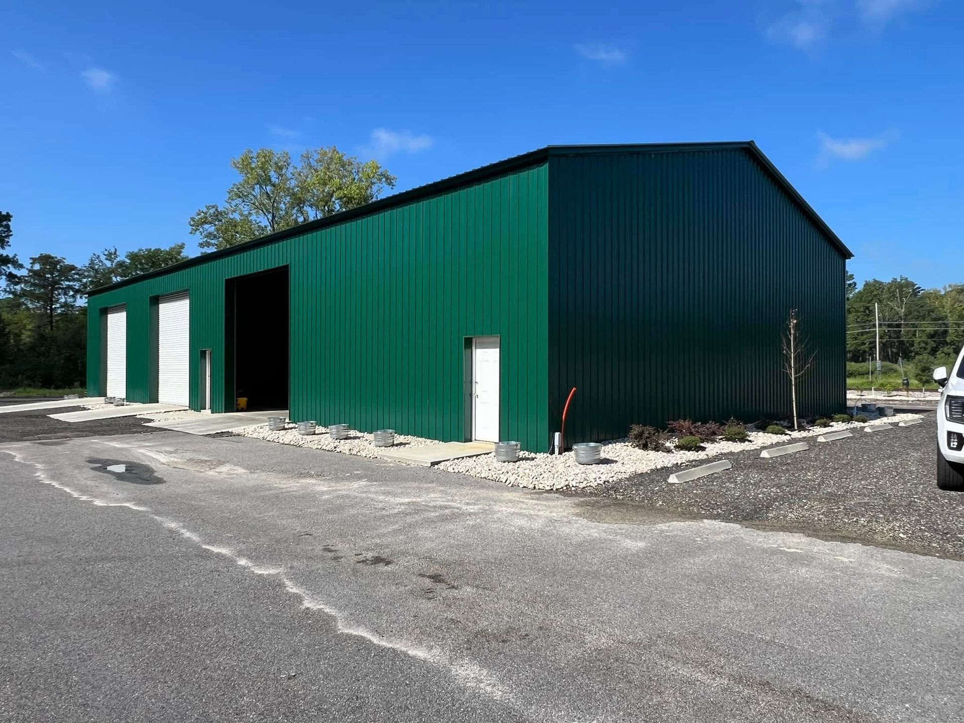Green metal industrial building with three garage doors and small white doors under a blue sky.