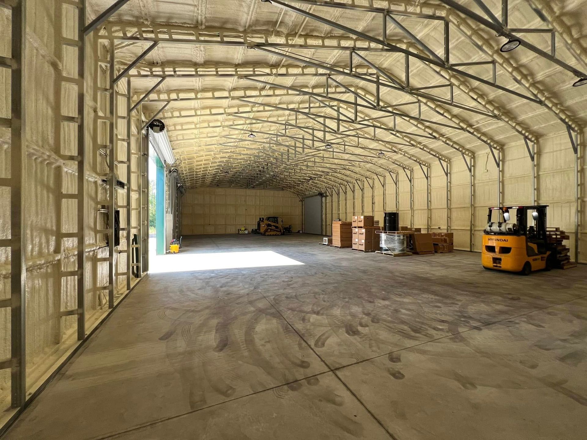 Interior of an empty warehouse with spray foam insulation. Metal framework supports the roof. A forklift and boxes are inside.