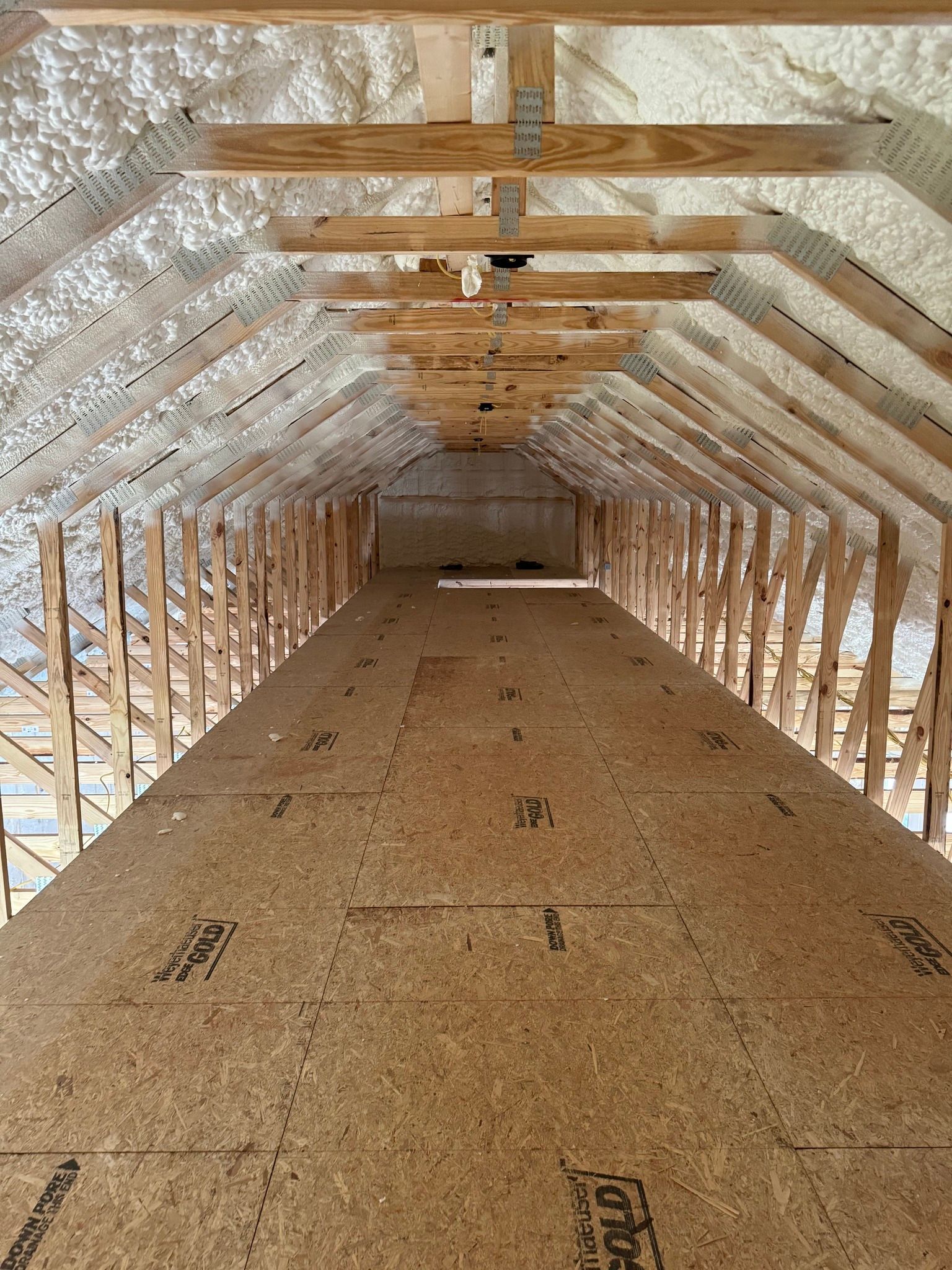 View of an attic space with wooden rafters and spray foam insulation. OSB flooring covers the floor.