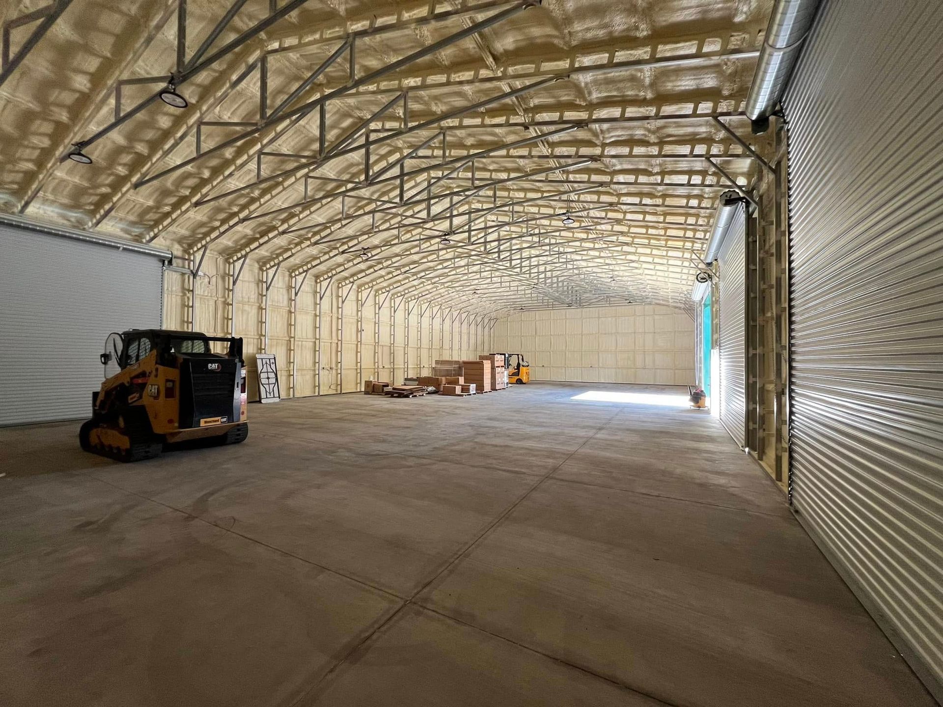 Interior of a large warehouse with spray foam insulation and a skid steer.
