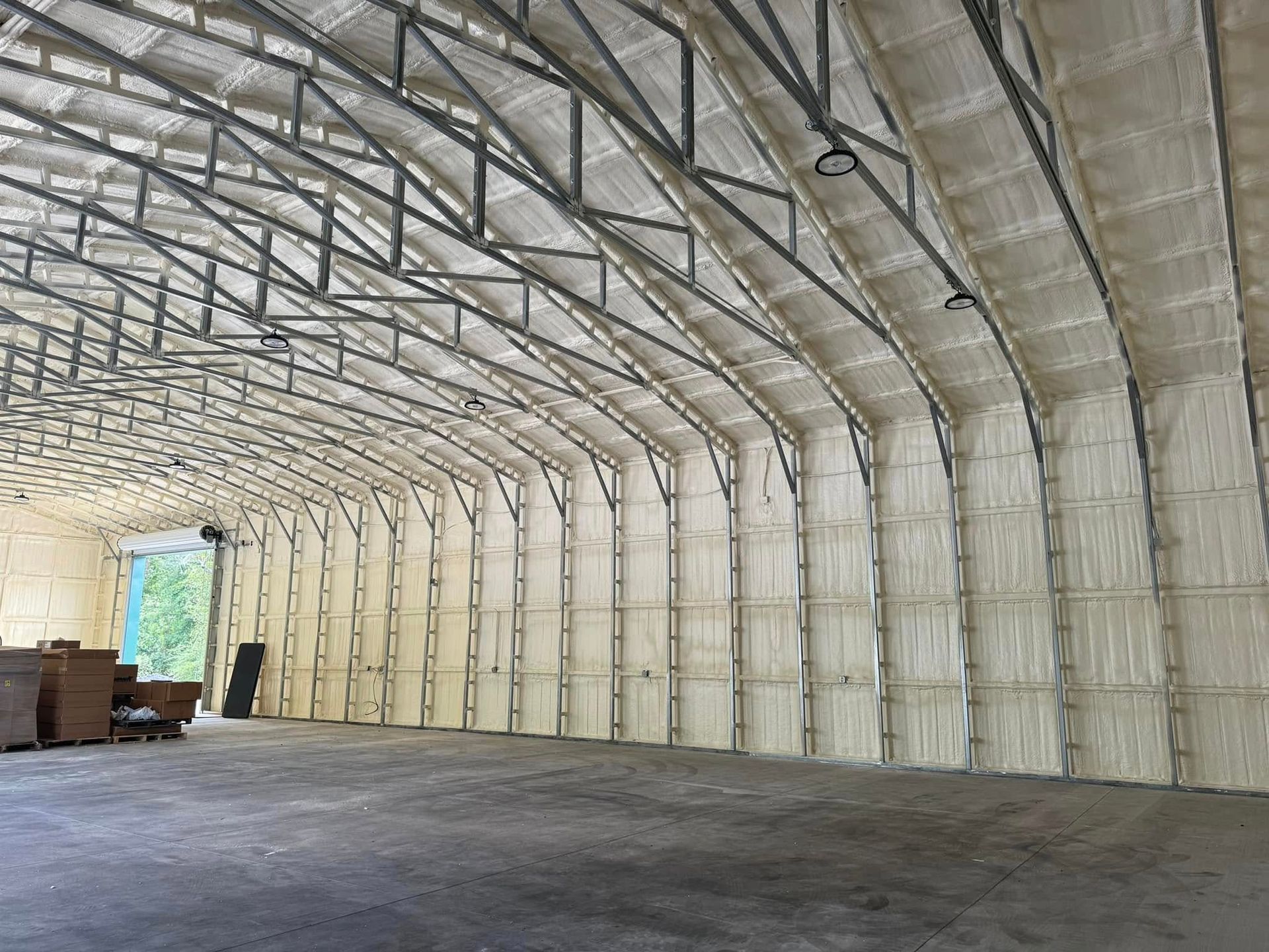 Interior of a large warehouse with curved metal beams and spray foam insulation on walls and ceiling.