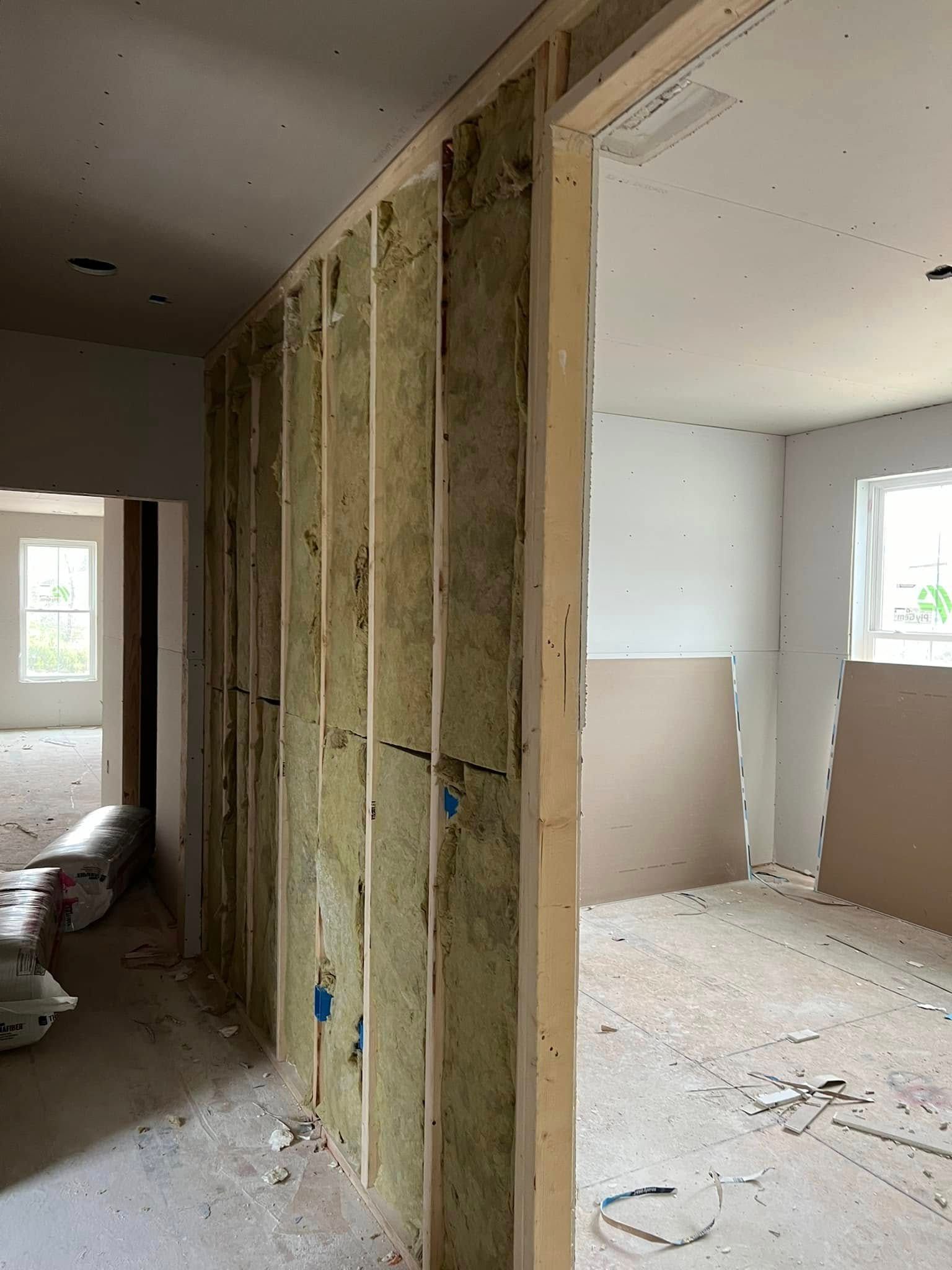 Interior view of a building under construction. Studs with insulation in a wall opening, unfinished drywall, light.