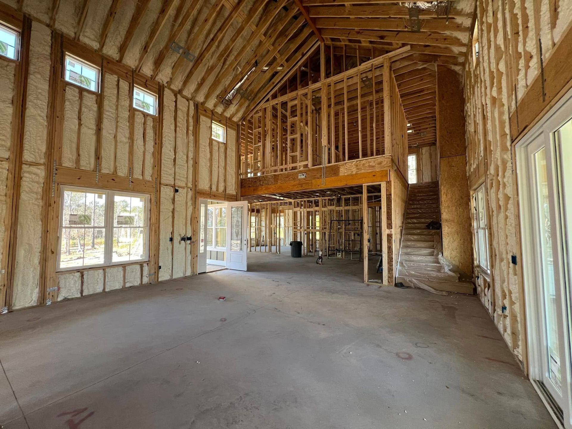 Interior view of a building under construction, showing wooden framing, spray foam insulation, and a second-story loft.