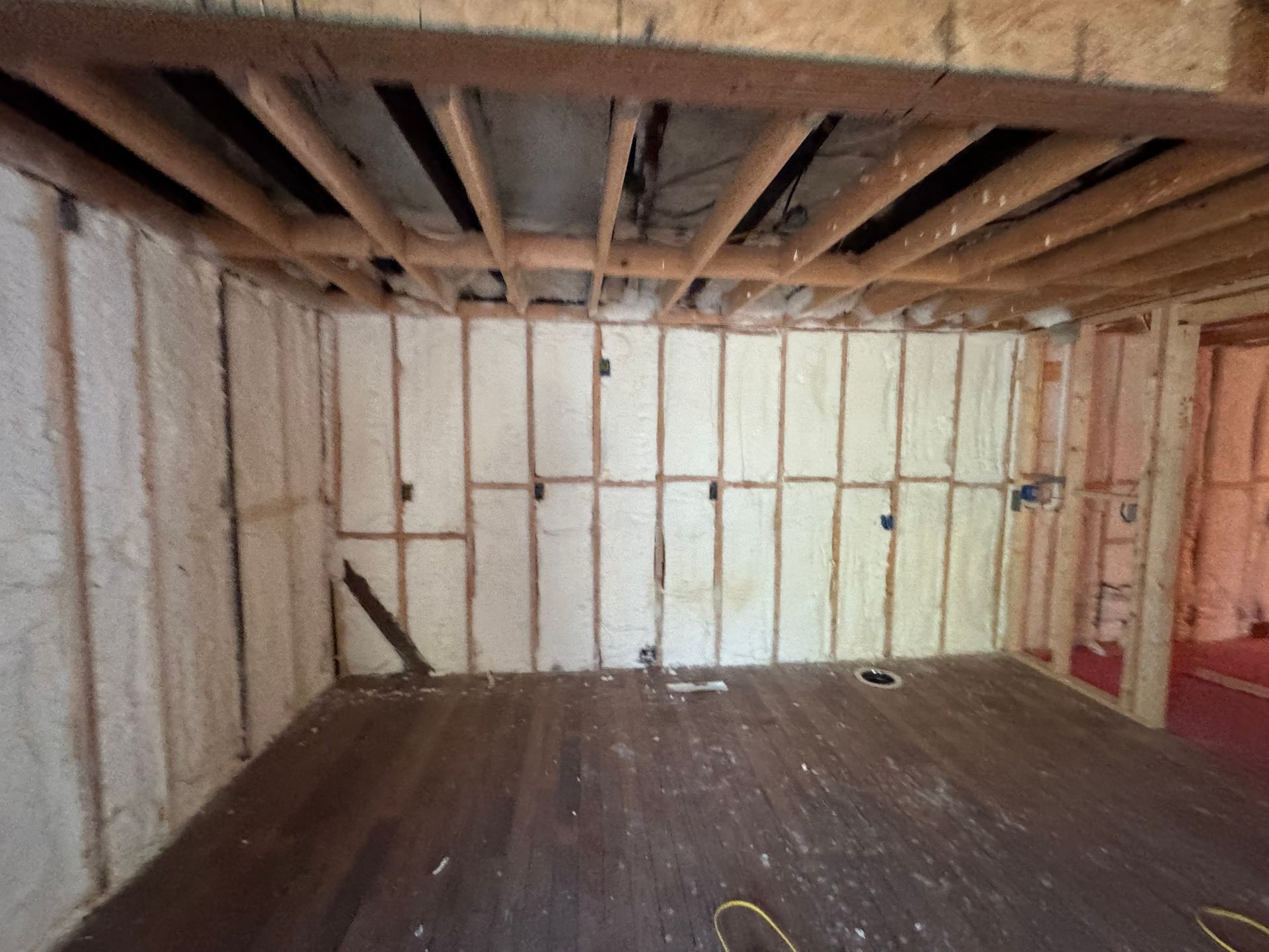 Interior room with exposed wood framing and white foam insulation on walls and ceiling. Dark wood floor.