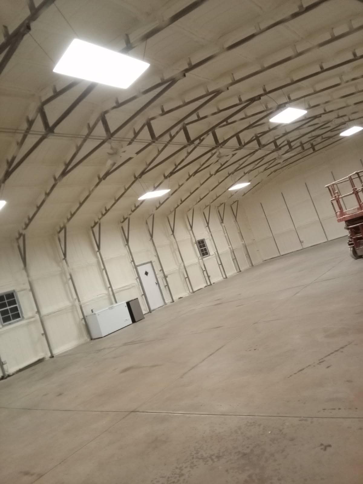Interior of a large warehouse with white walls, skylights, and a curved ceiling. A forklift is visible on the right.