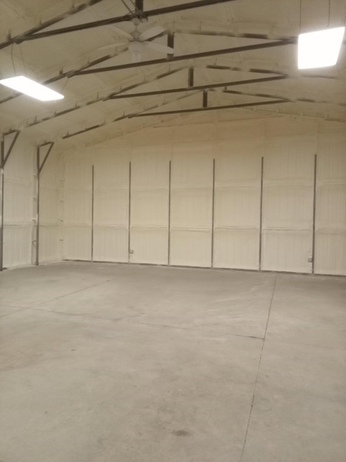 Empty warehouse interior with concrete floor, white walls, and exposed metal beams.