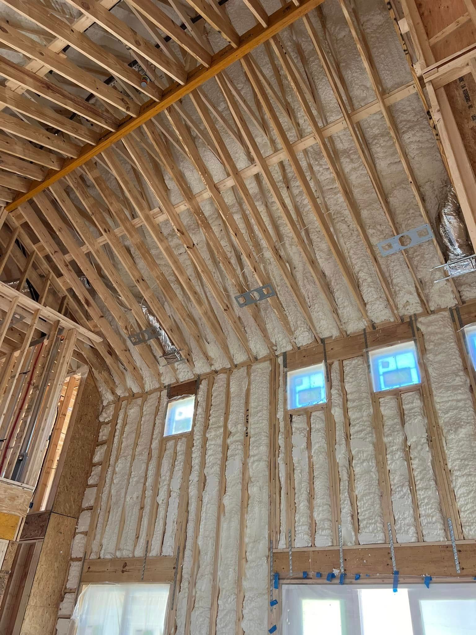 Interior of a building under construction, with spray foam insulation between wooden beams and framing.