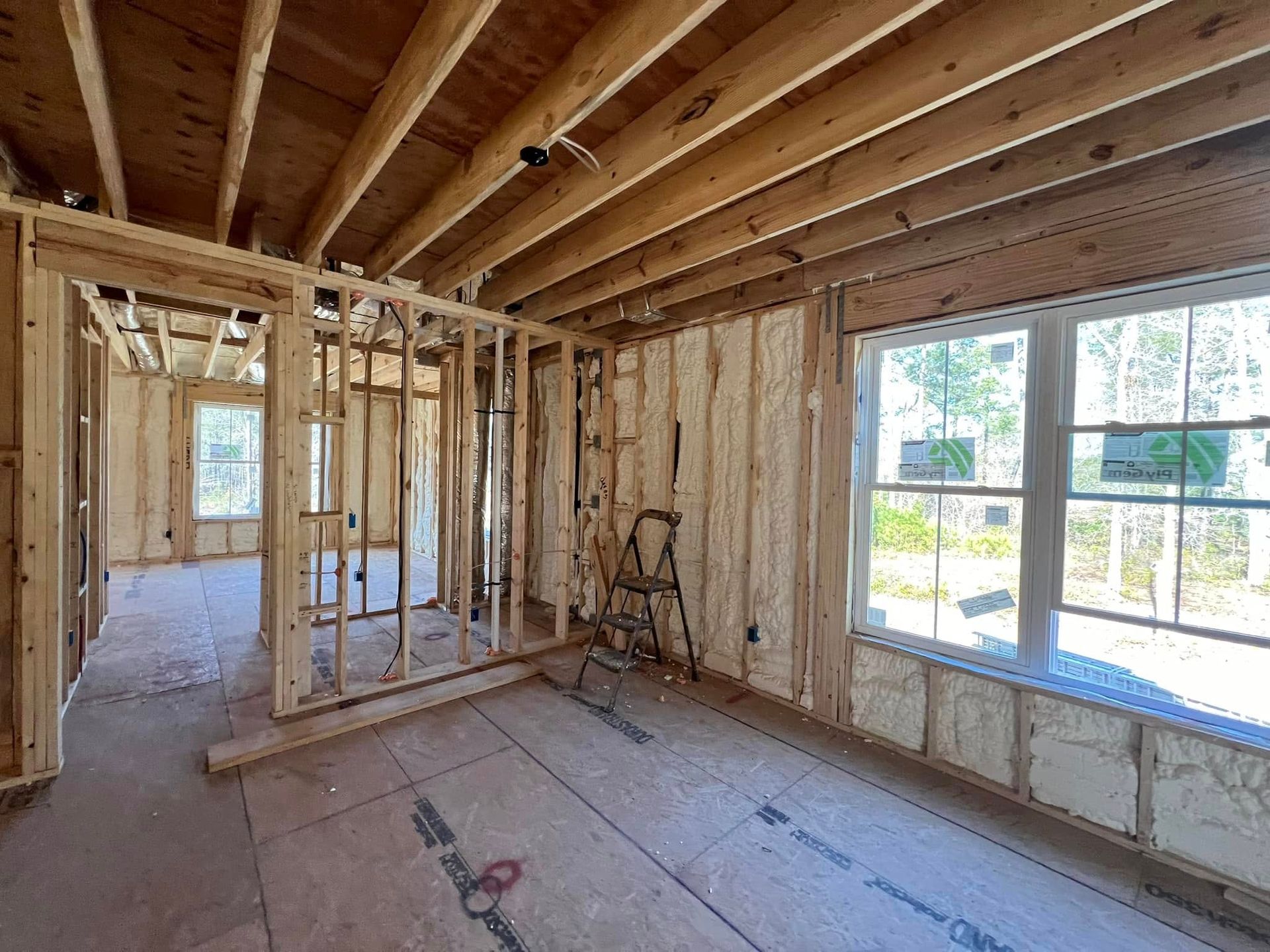 Interior view of a new home under construction with exposed wooden framing and spray foam insulation.
