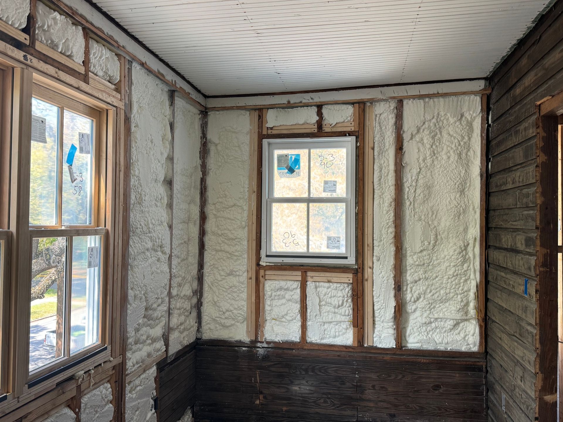 Interior room with spray foam insulation between wooden studs, near windows.