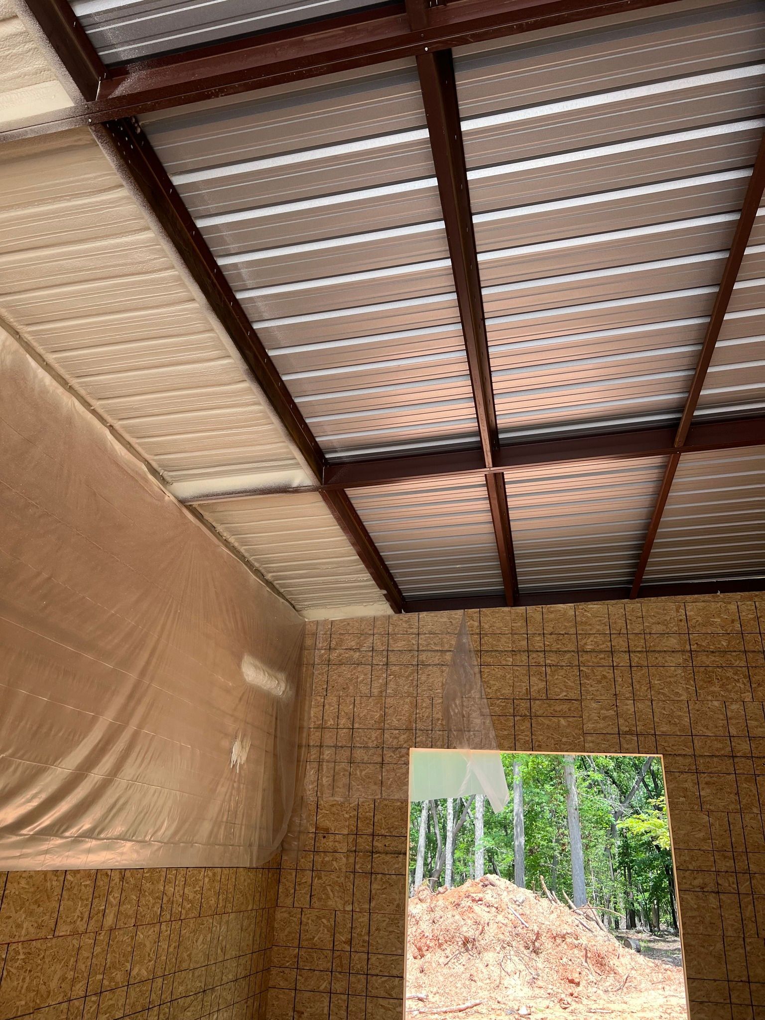 Interior view of a building under construction, showing a metal roof frame, insulation, and unfinished walls with an open doorway.
