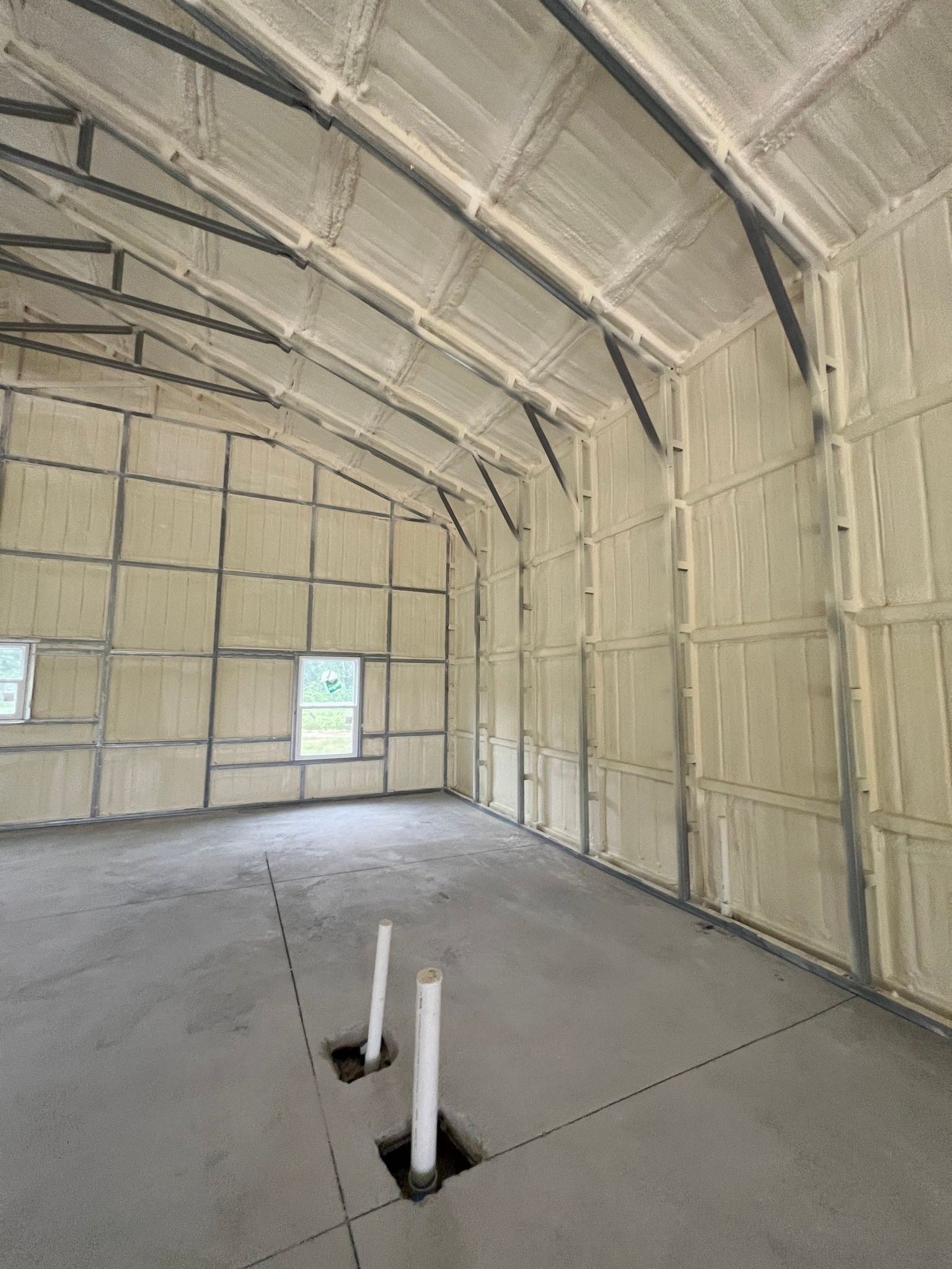 Interior view of a building with spray foam insulation on walls and ceiling. Concrete floor with plumbing visible.