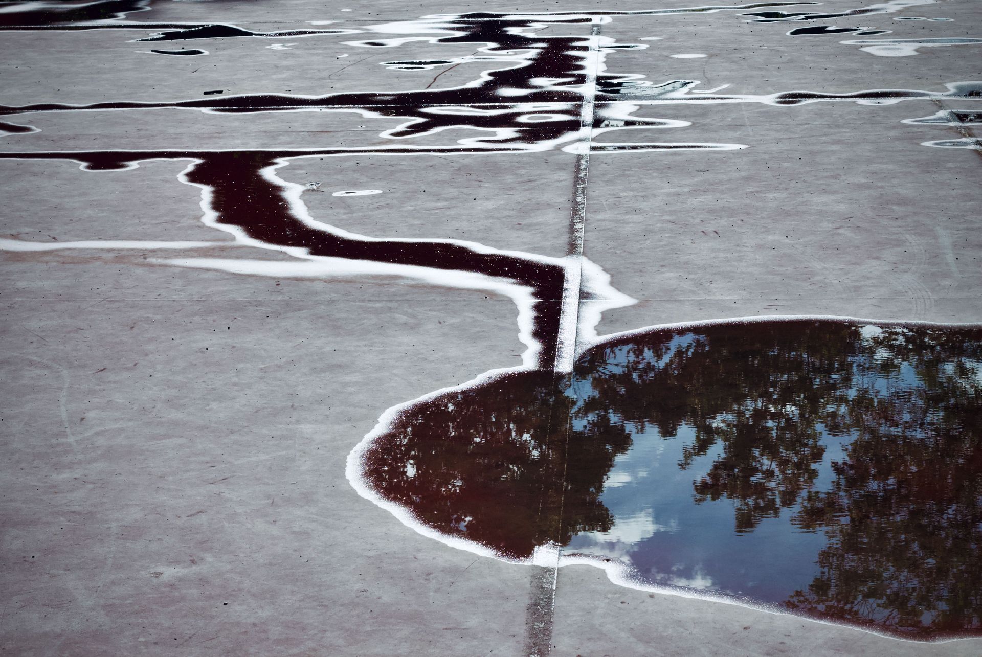 Shallow puddles reflecting clouds on a cracked concrete surface
