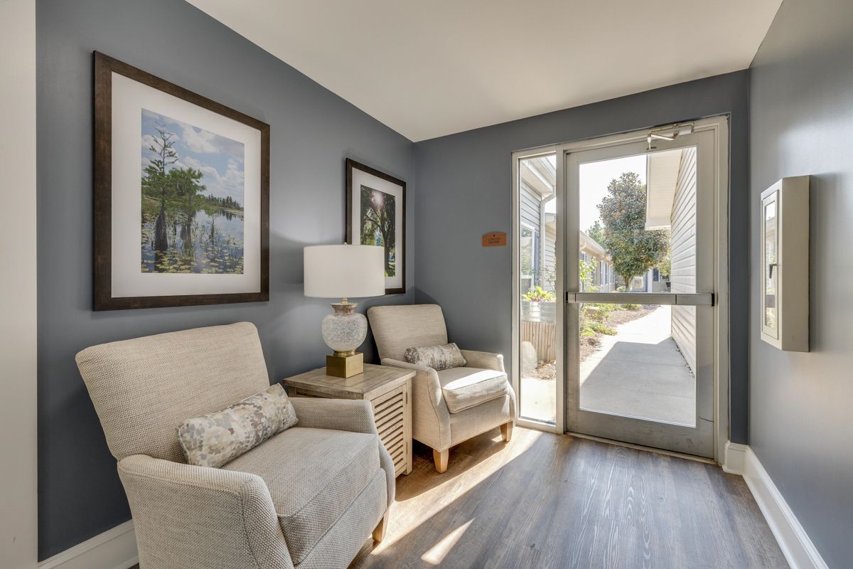 A living room with two chairs , a table , a lamp and a door.
