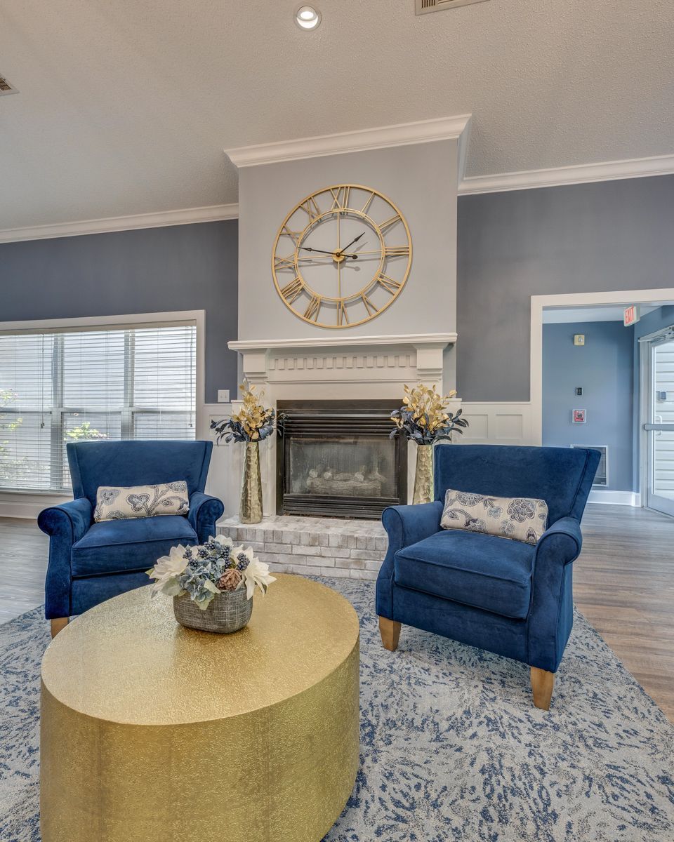 A living room with a fireplace , chairs , a coffee table and a clock on the wall.