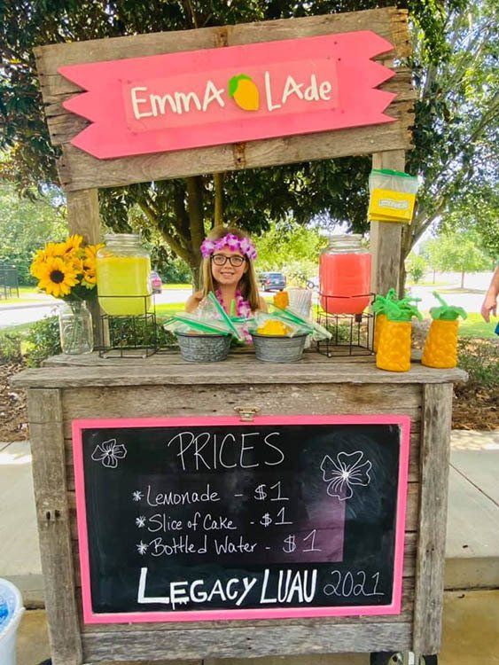 A girl is standing behind a lemonade stand.
