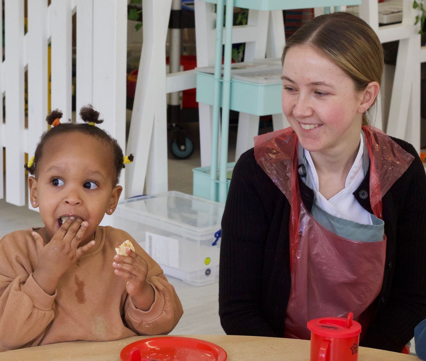 Child eating snack at nursery with Nursery Nurse