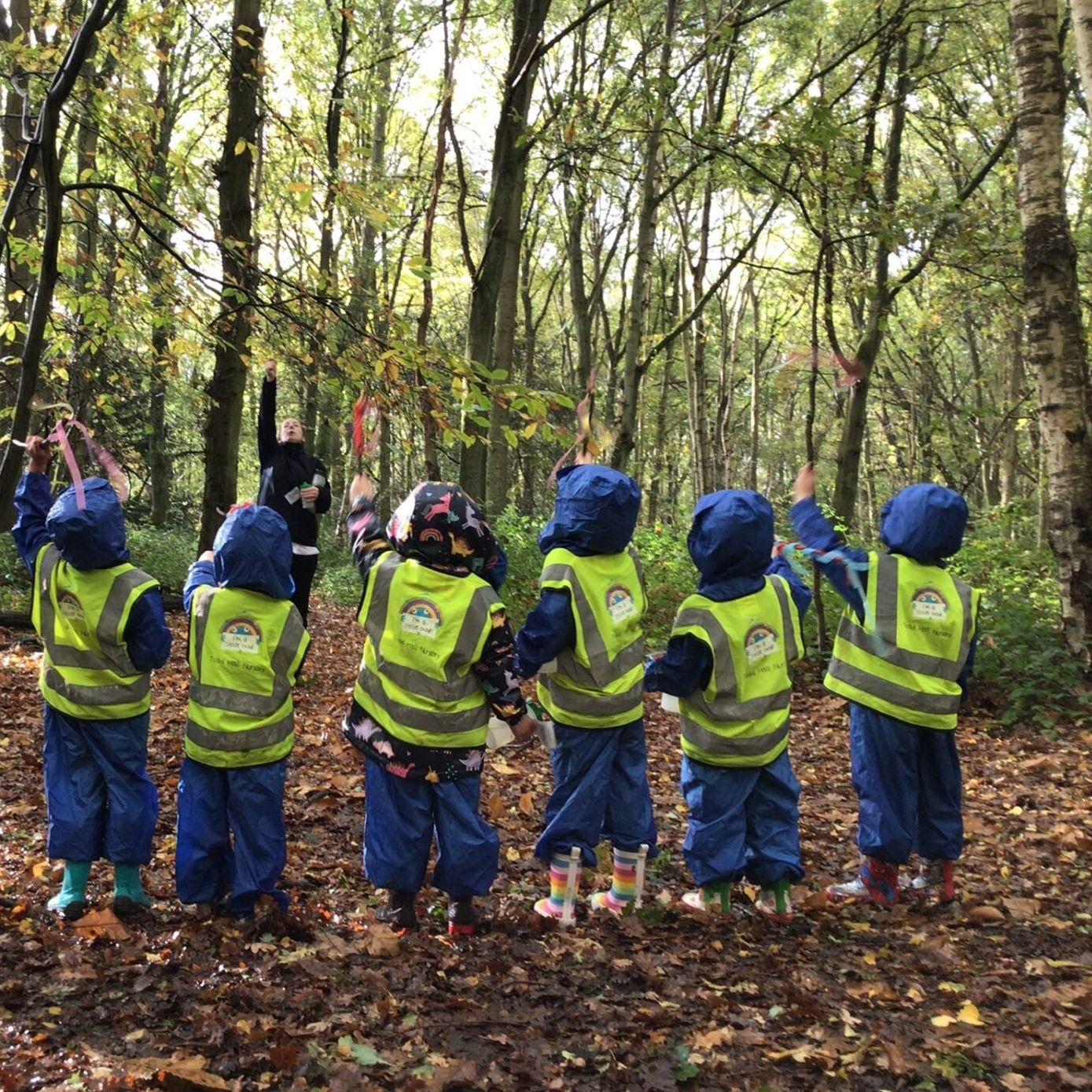A group of children wearing safety vests are standing in the woods.