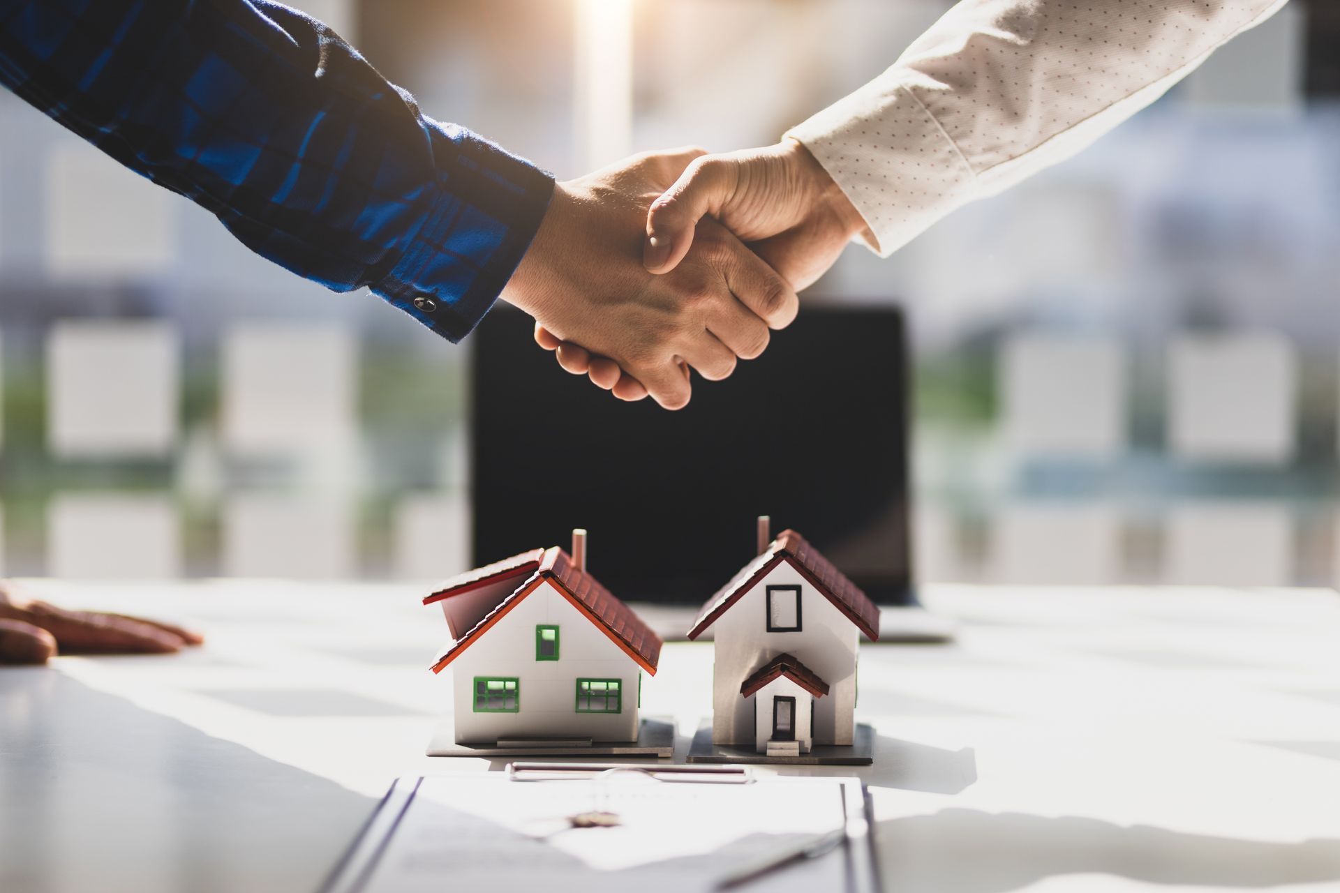 Two people shaking hands over small model houses on a desk.