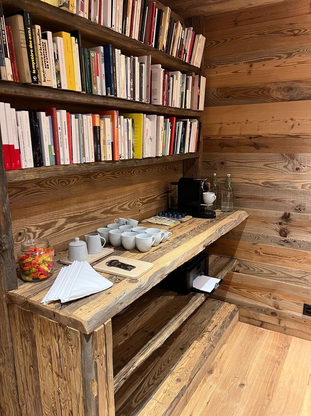 Une étagère en bois avec des rangées de livres au-dessus d'un comptoir où se trouvent des tasses, une machine à café et un bocal de bonbons colorés.