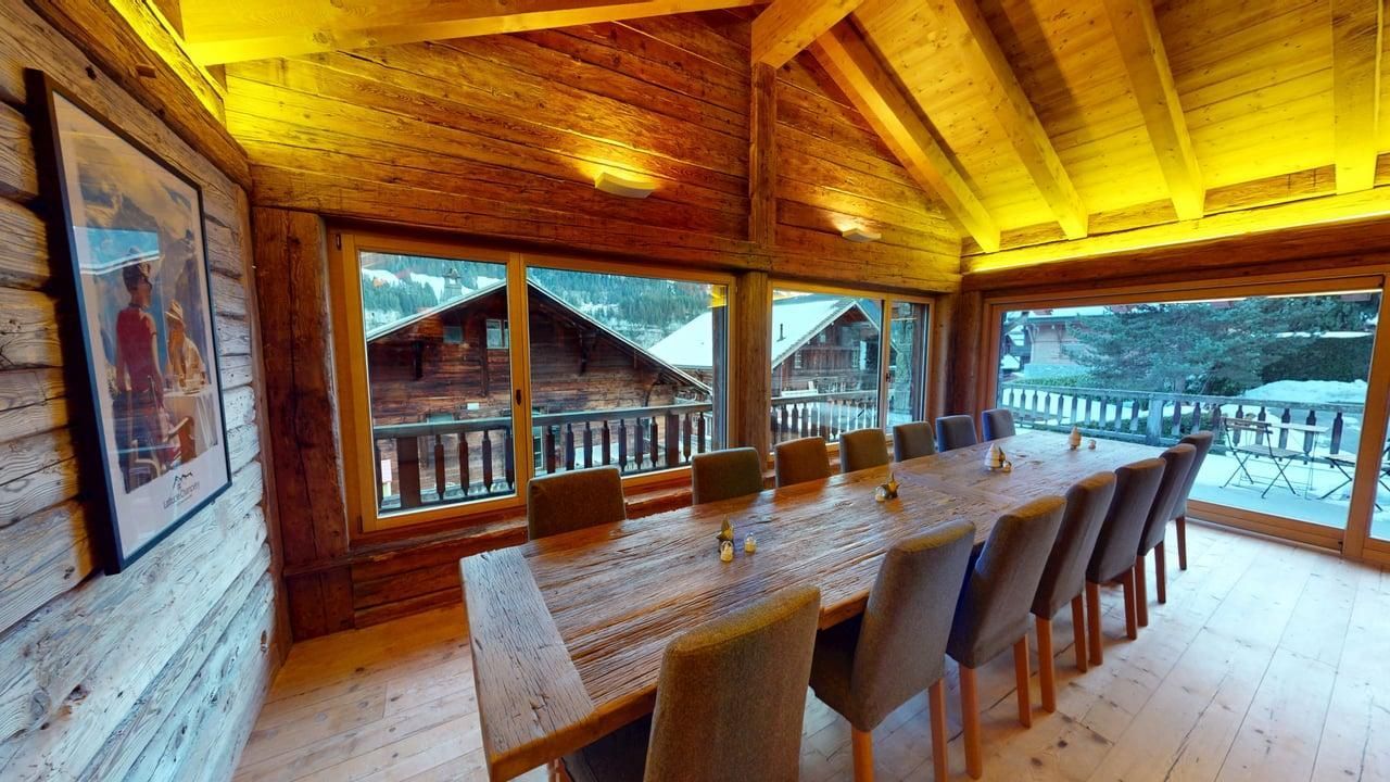 Salle à manger lambrissée avec une longue table, des chaises et de grandes fenêtres donnant sur un paysage enneigé