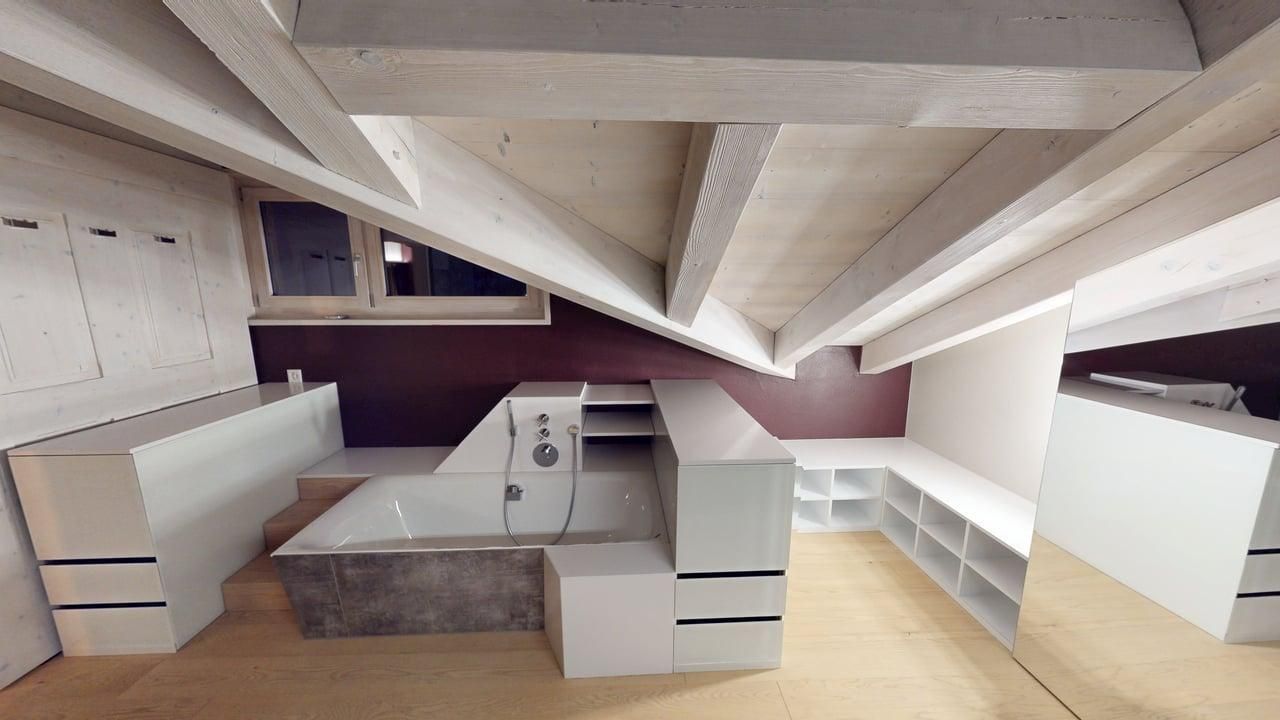 Modern attic bathroom with white built-in storage, a sunken bathtub, wood-paneled sloped ceiling, and large mirror.
