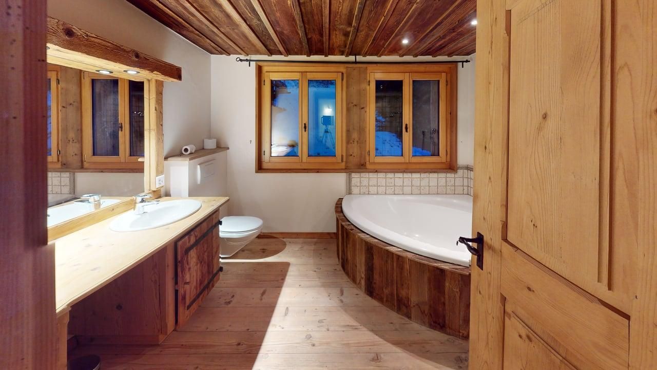 A rustic bathroom with wood paneling, a double vanity, a corner soaking tub, and windows with outdoor views.