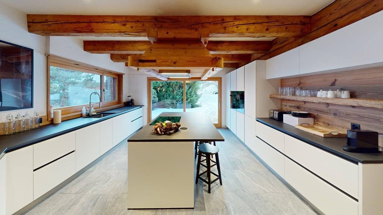 Modern kitchen with light cabinets, dark countertops, wooden ceiling beams, and a central island with stools.