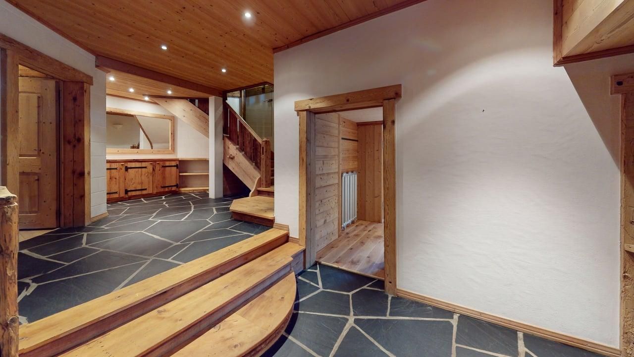 An interior hallway featuring a stone floor, wooden stairs, and a door leading to a small room with light wood walls.