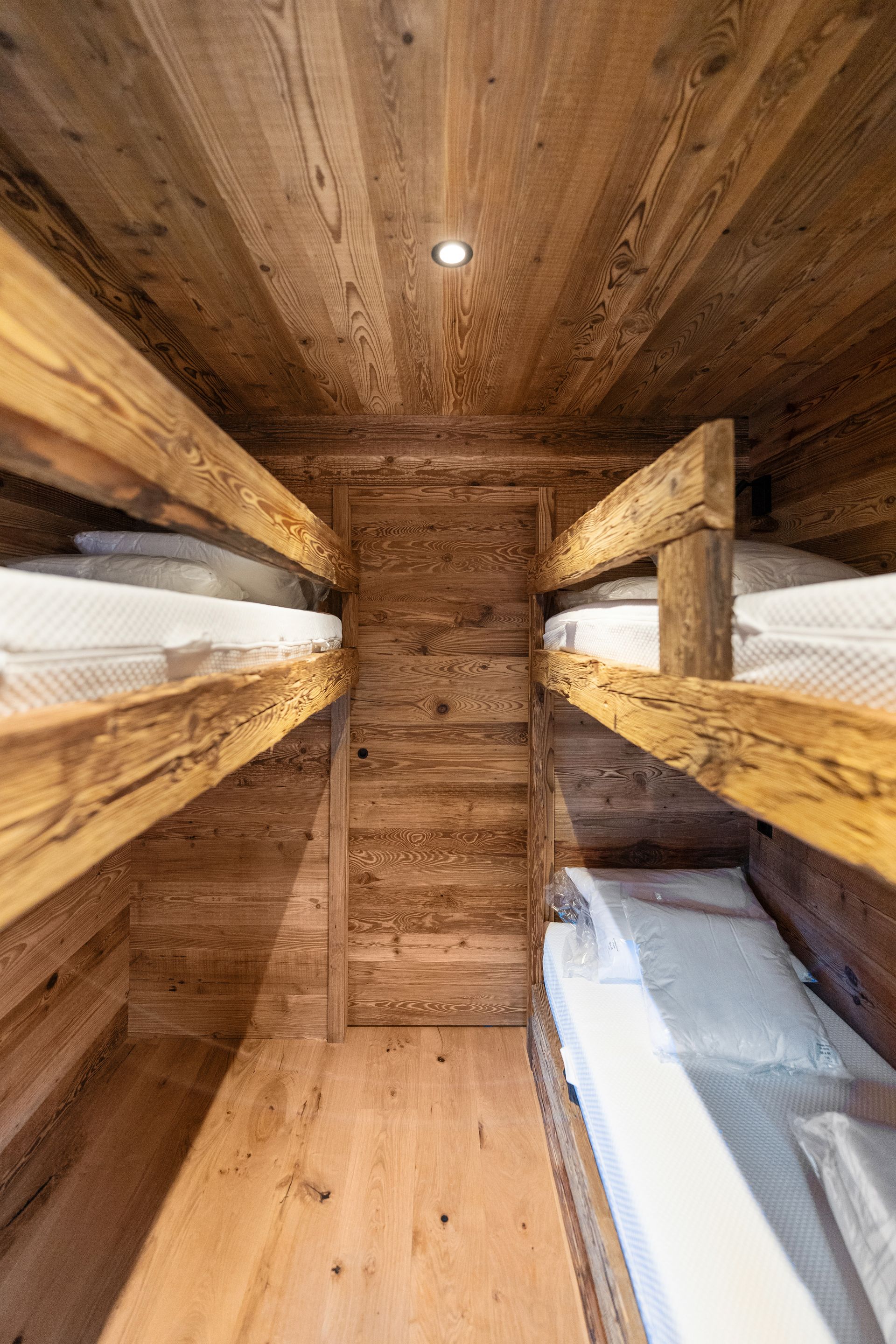 A small rustic room with two sets of built-in wooden bunk beds facing each other, featuring warm-toned pine paneling.