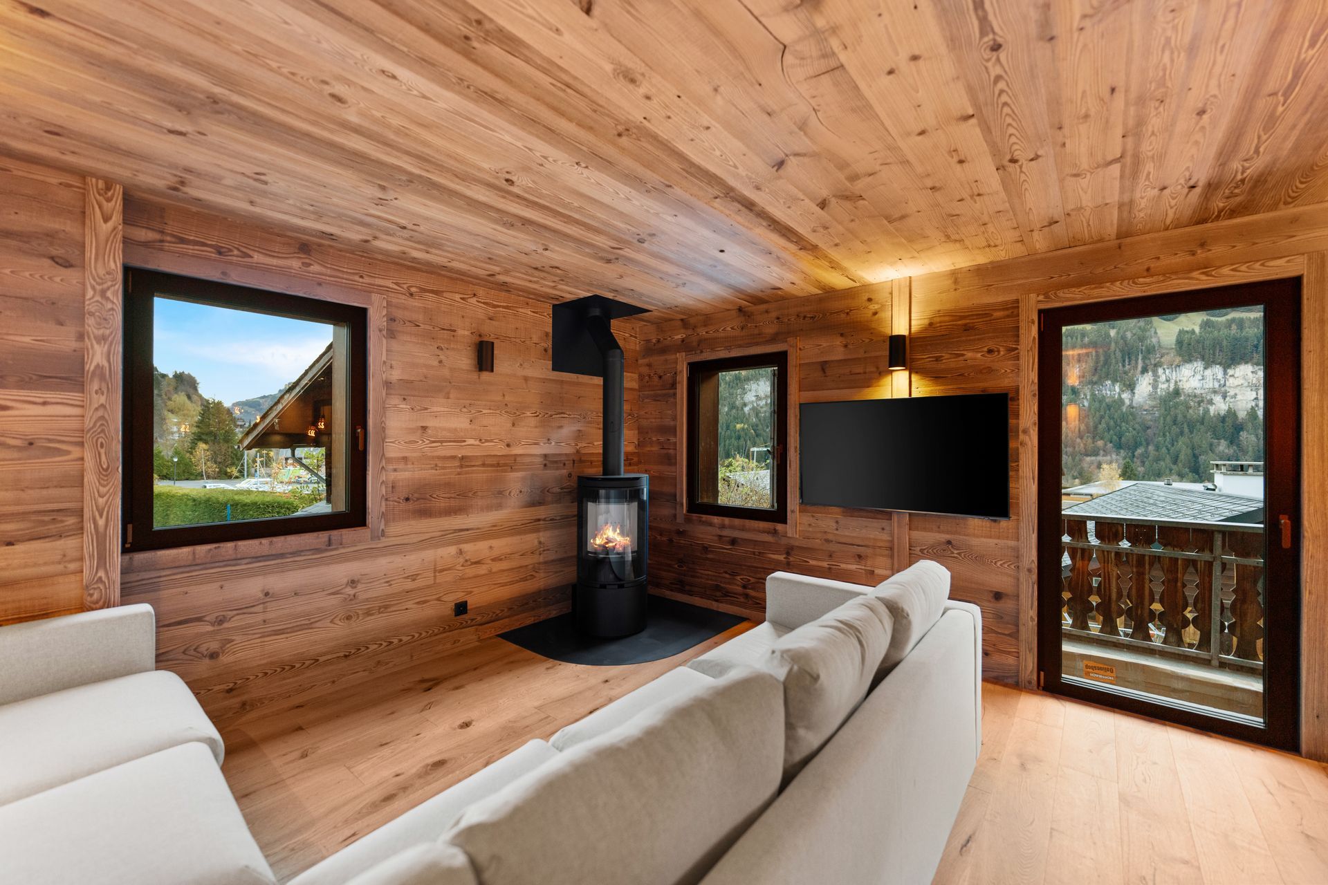 Chambre confortable aux murs lambrissés, avec cheminée, canapé blanc et télévision murale donnant sur la montagne.