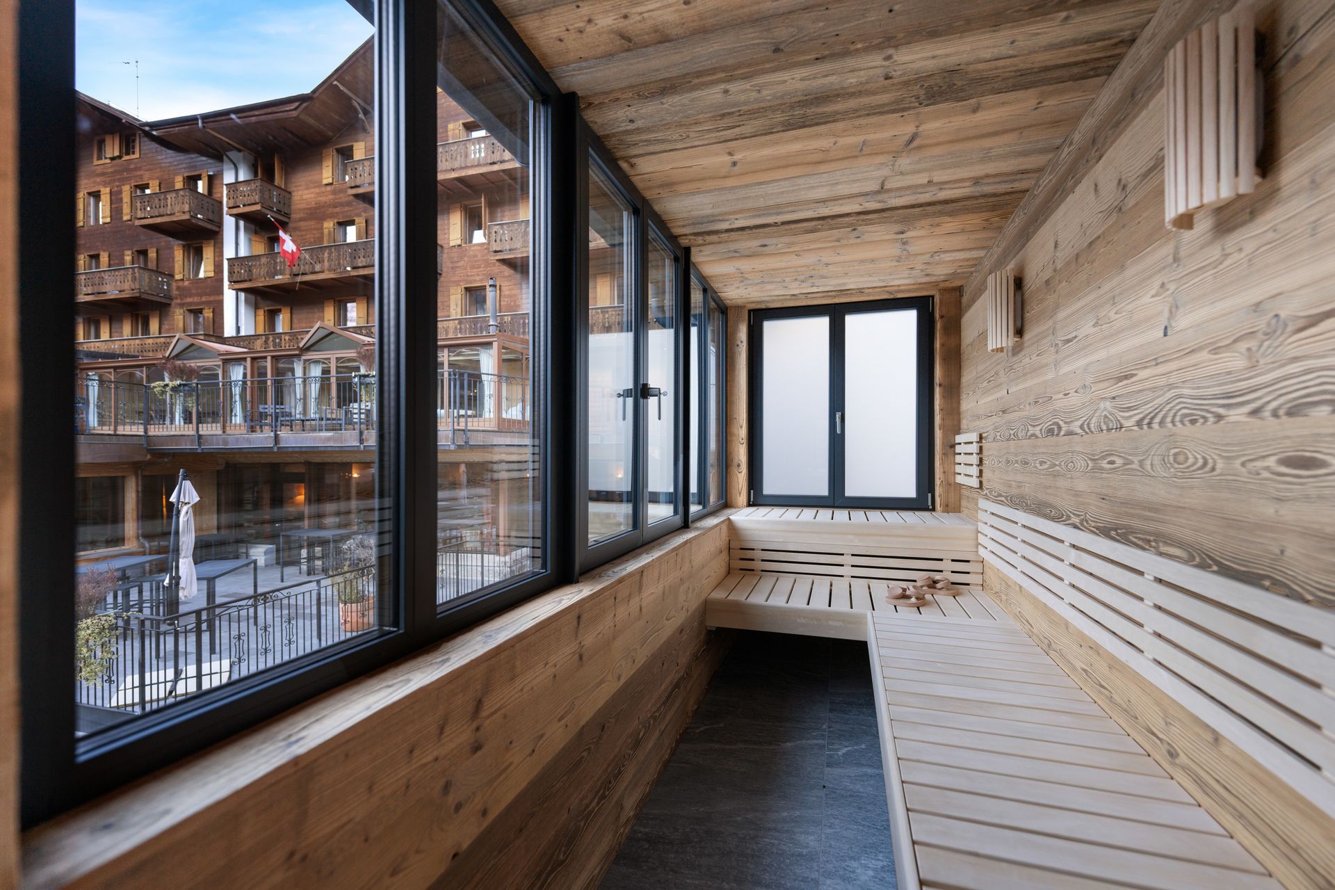 A wooden sauna with a large window overlooking a hotel courtyard.