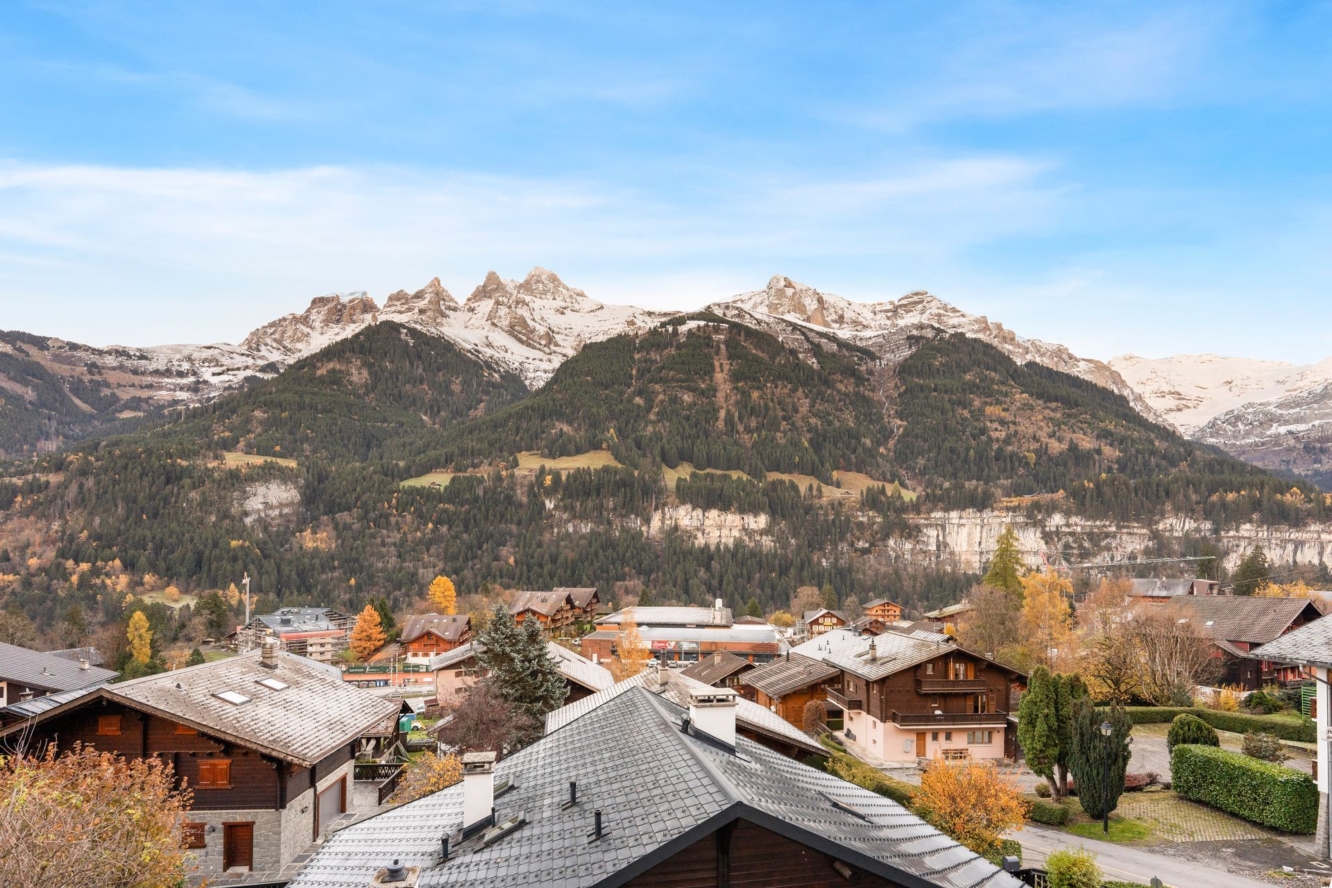 A mountain village nestled below a range of snow-capped peaks under a bright blue sky.