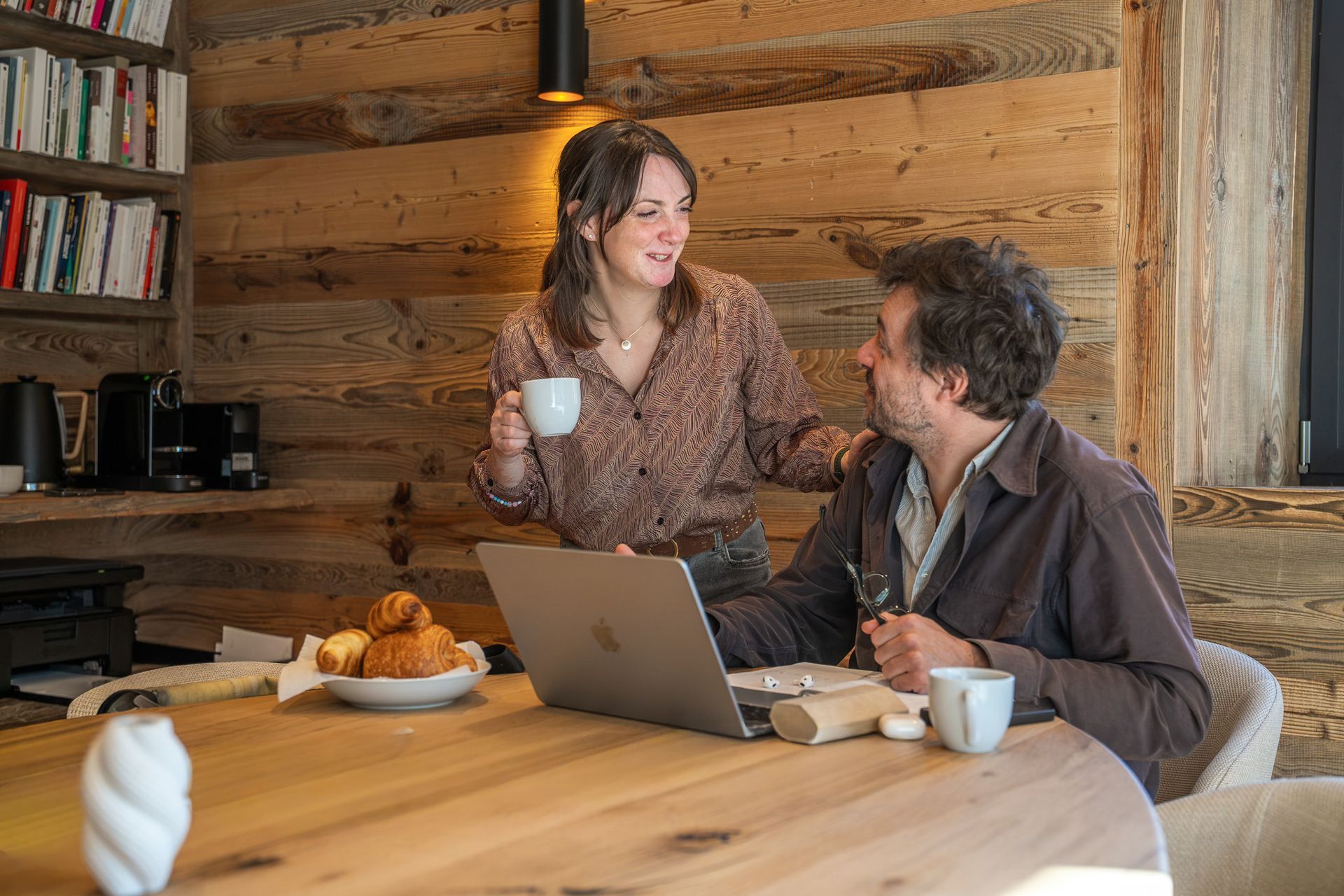 Two people chatting at a wooden table with laptops and coffee in a cozy rustic café