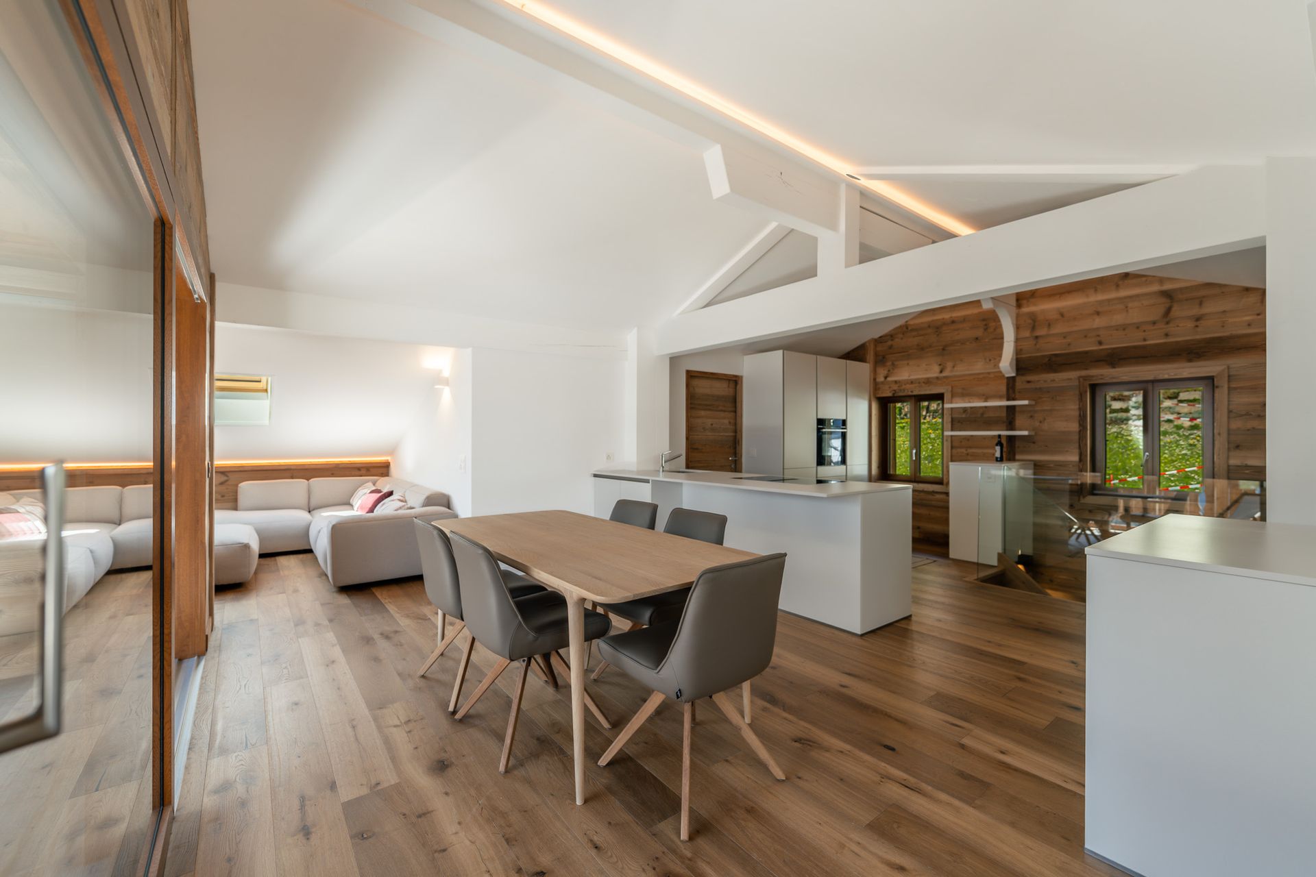 A modern, open-concept living space with a dining set, white kitchen island, and cozy seating area on hardwood floors.