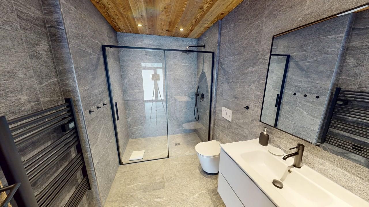 Une salle de bains moderne avec des murs carrelés de pierre grise, une douche à l'italienne en verre, un lavabo blanc et un plafond lambrissé.