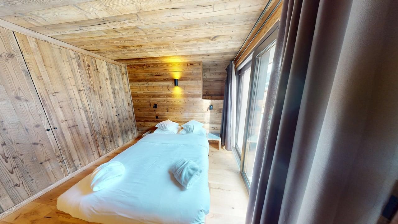 Une chambre confortable avec des lambris clairs aux murs et au plafond, un lit blanc et de grandes fenêtres en verre.