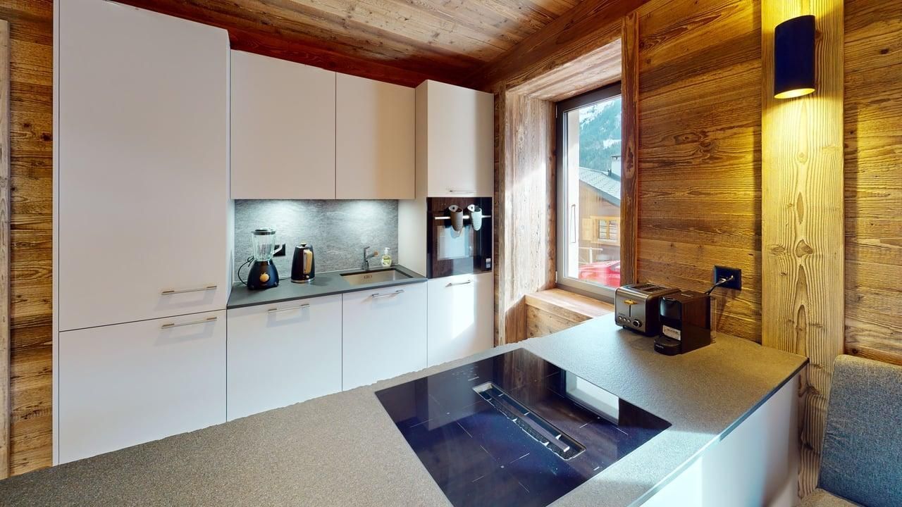 Une cuisine blanche moderne avec des murs en bois, une plaque de cuisson intégrée et des appareils électroménagers dans un cadre de chalet rustique.