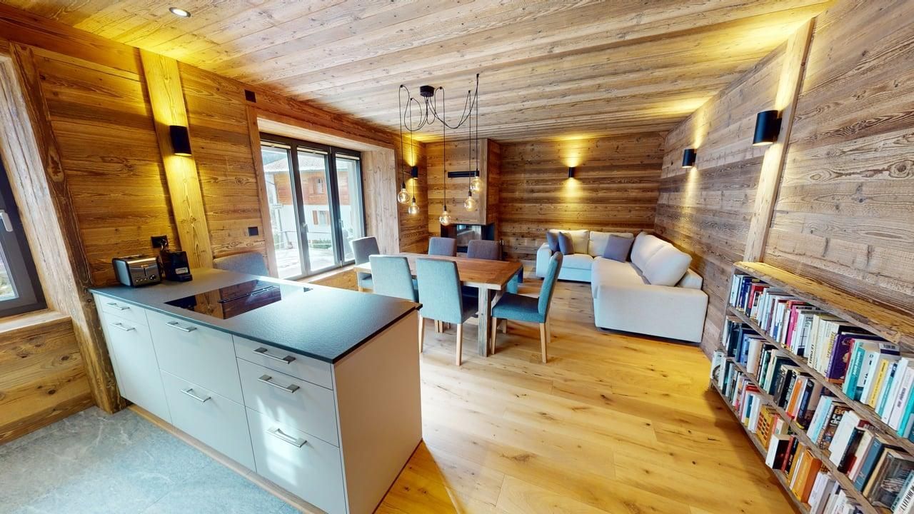 Une pièce de chalet moderne en bois à aire ouverte avec un îlot de cuisine, un coin repas, un canapé et un mur d'étagères.